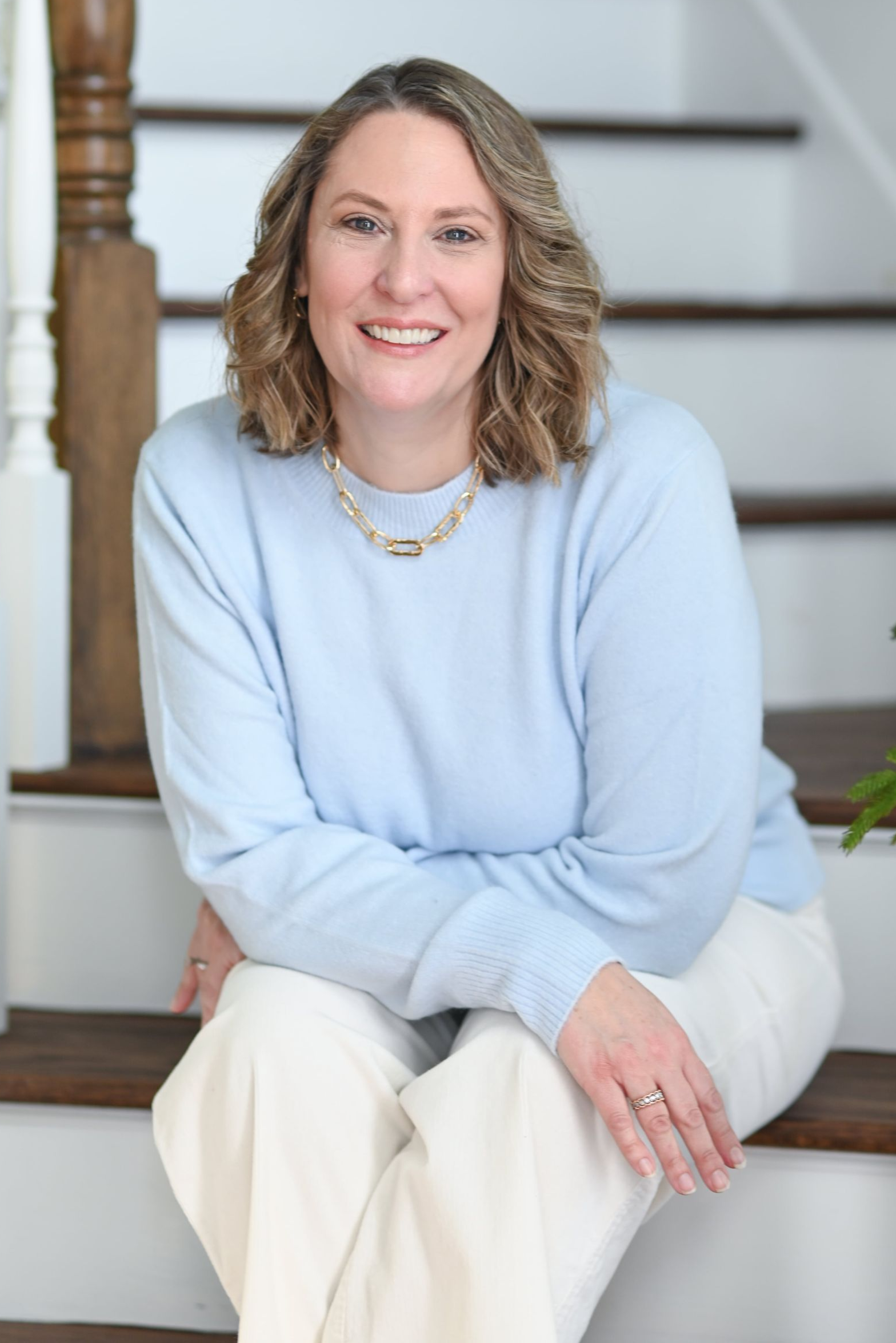 Woman smiling, wearing a burgundy leather jacket and cream-colored blouse, standing in front of a stone wall.