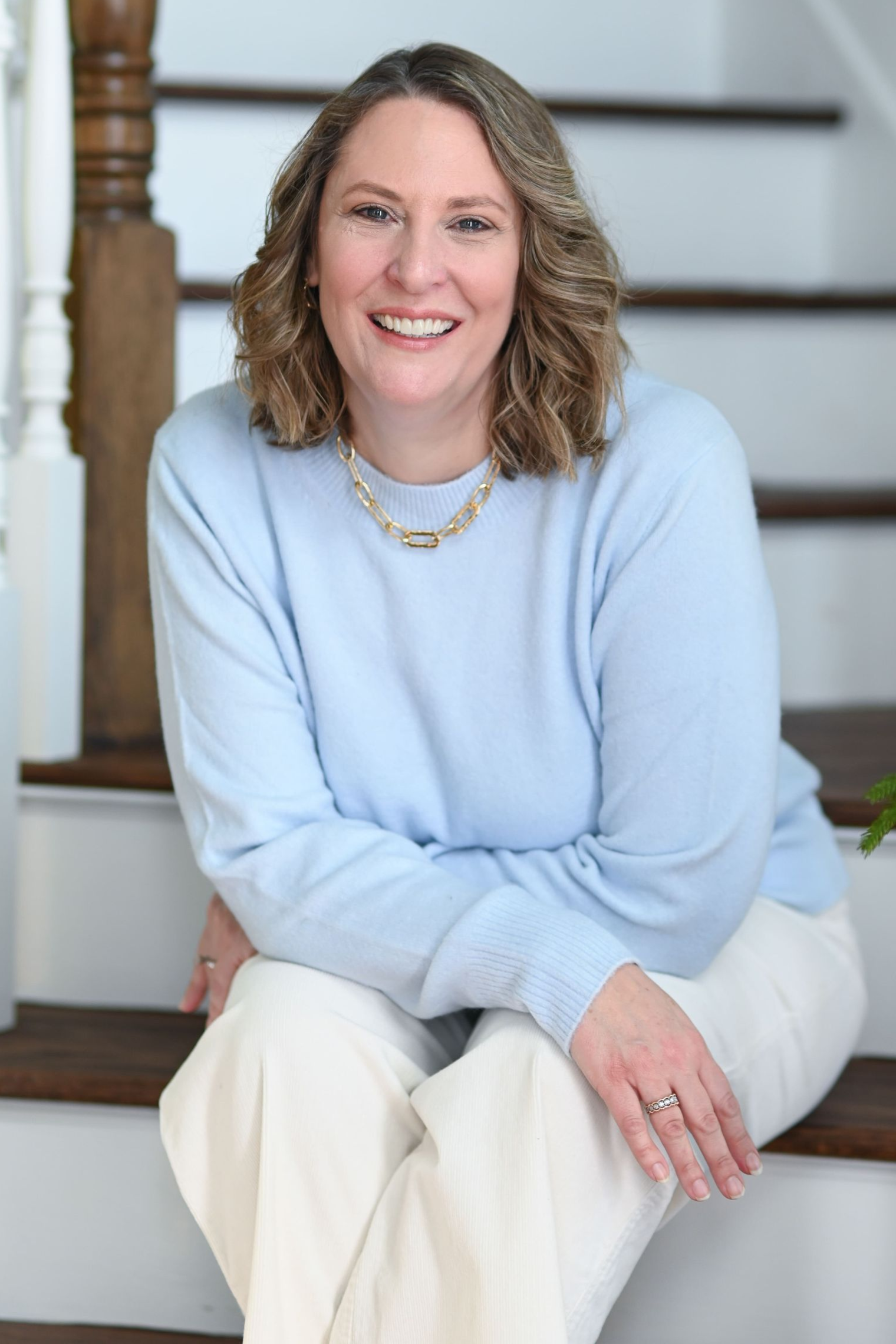 Woman smiling, wearing a burgundy leather jacket and cream-colored blouse, standing in front of a stone wall.