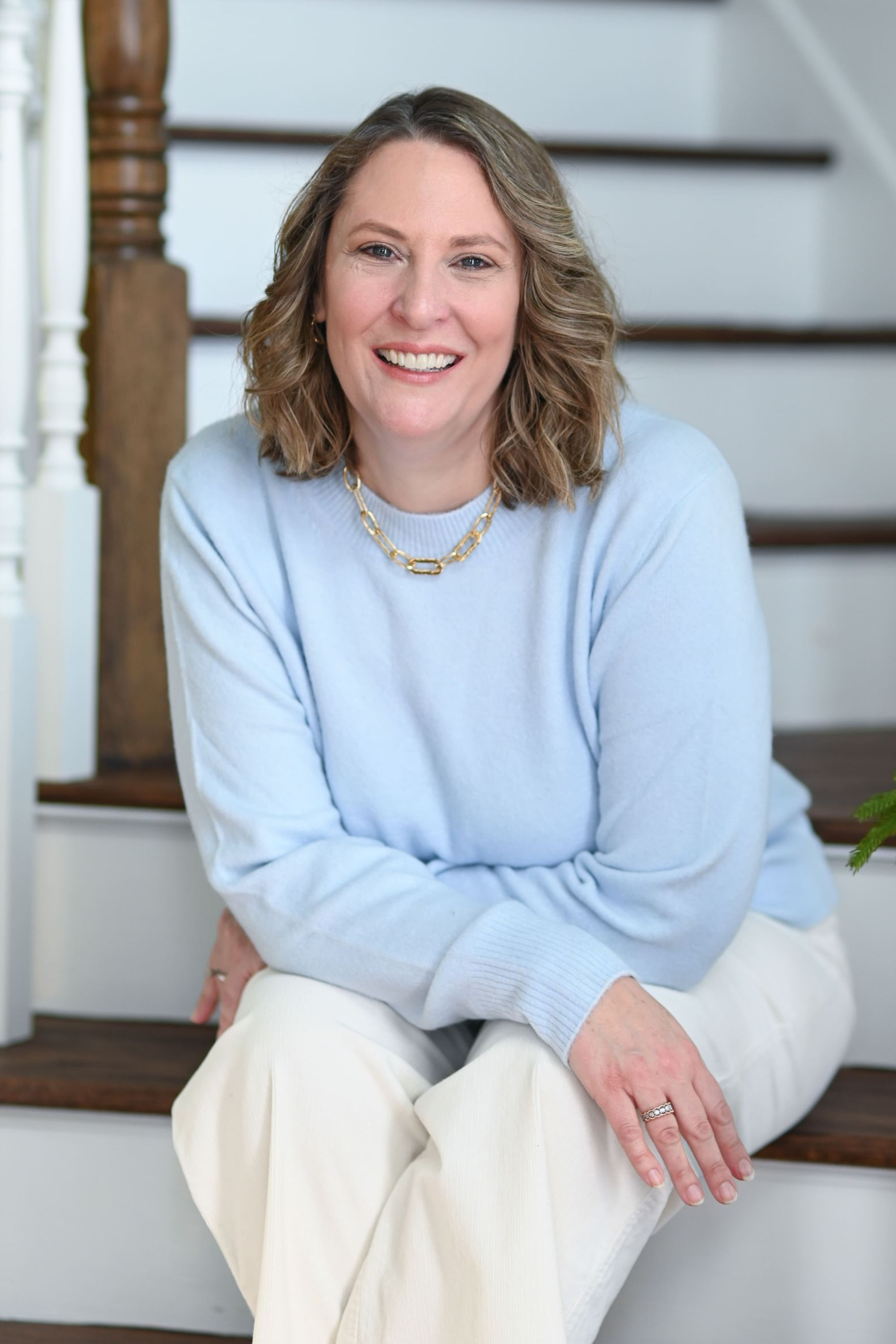 Woman smiling in front of a stone wall, wearing a maroon leather jacket and cream blouse.
