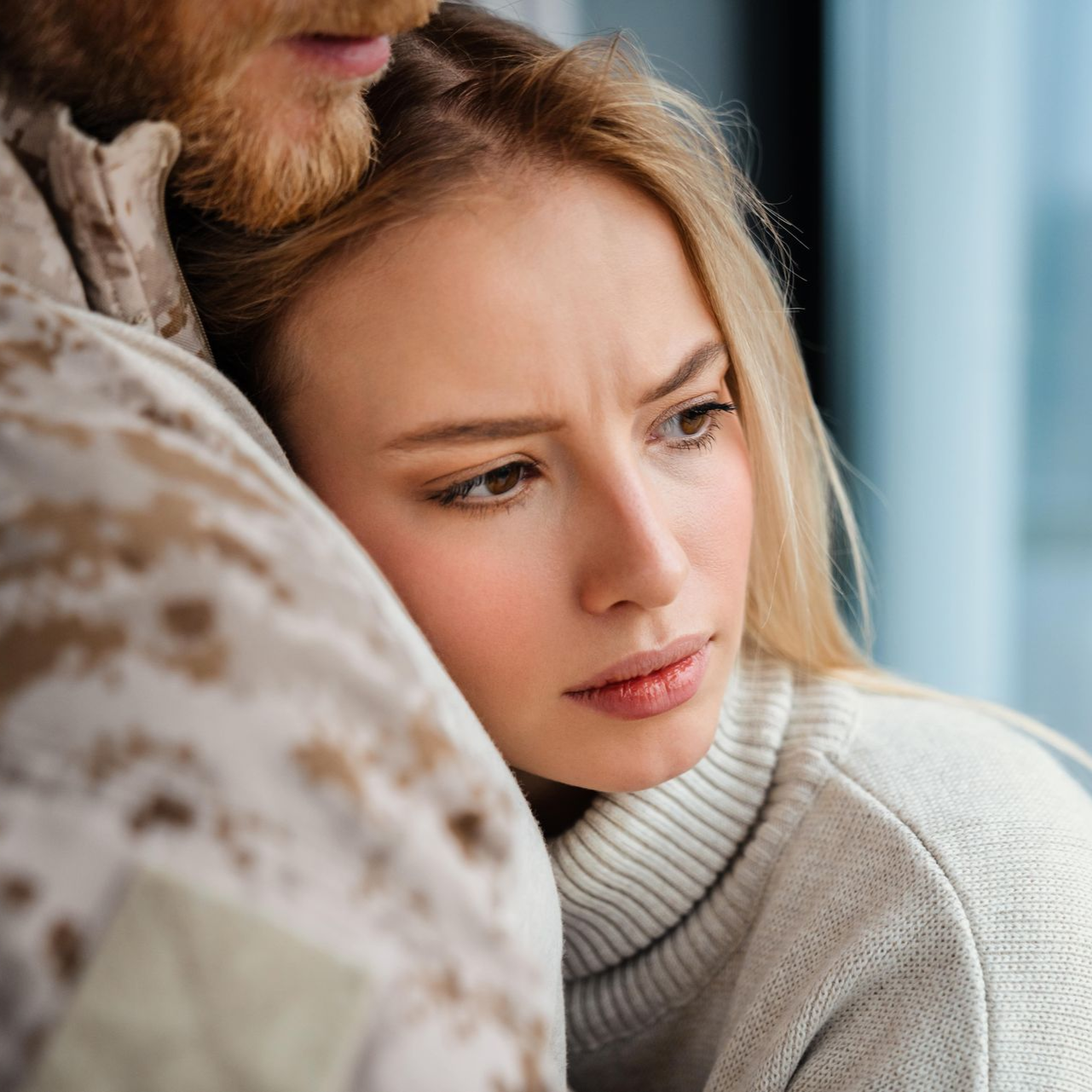 Woman leans on person in military uniform, looking worried.