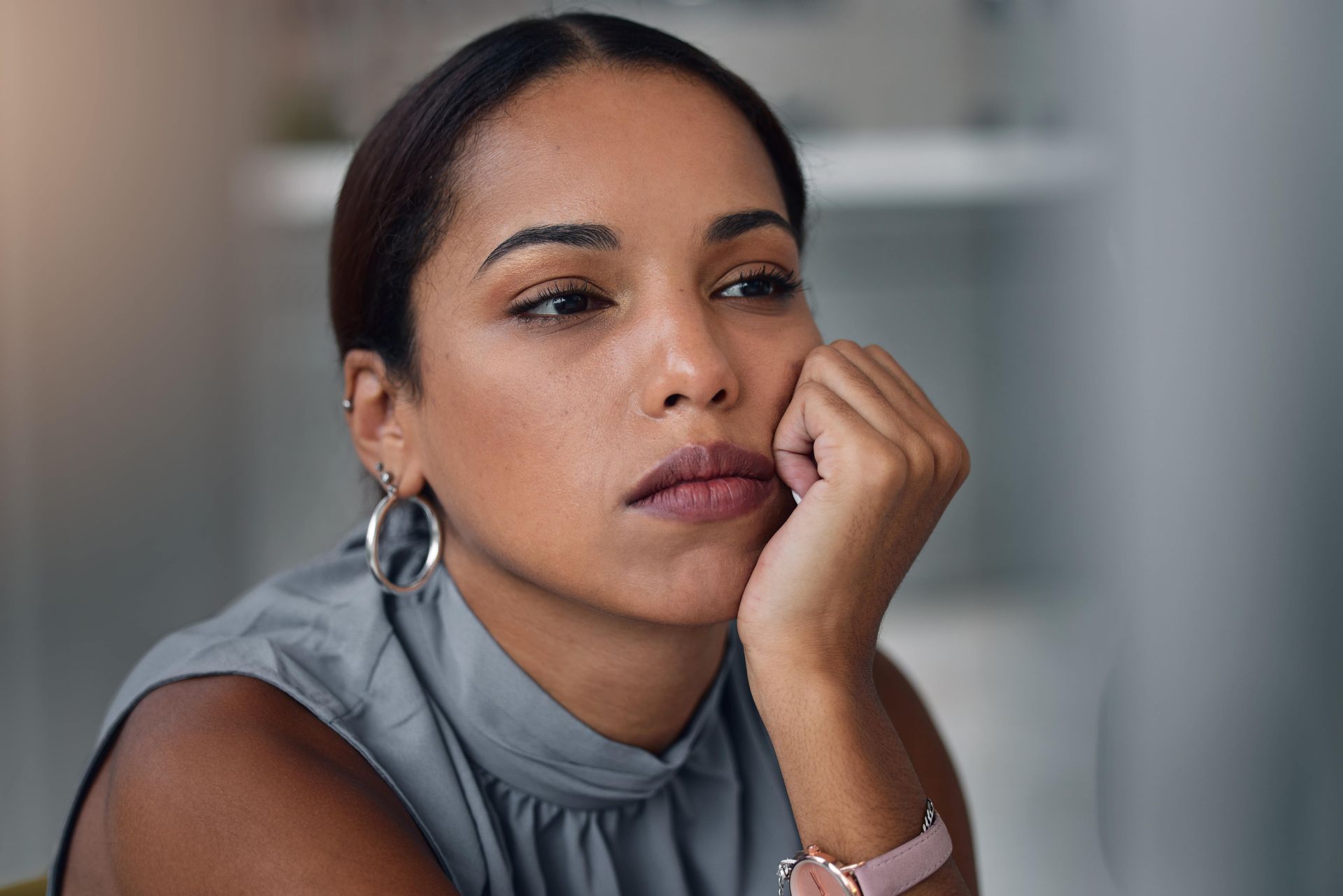 Woman resting chin on hand, looking thoughtful, indoors.