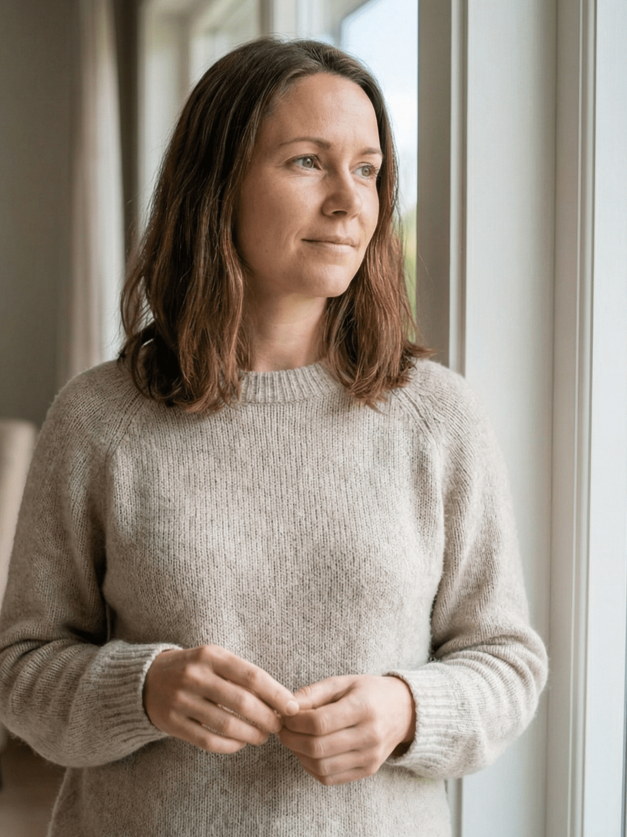 Woman in blue top sits on a gray couch, looking towards right; bright room.
