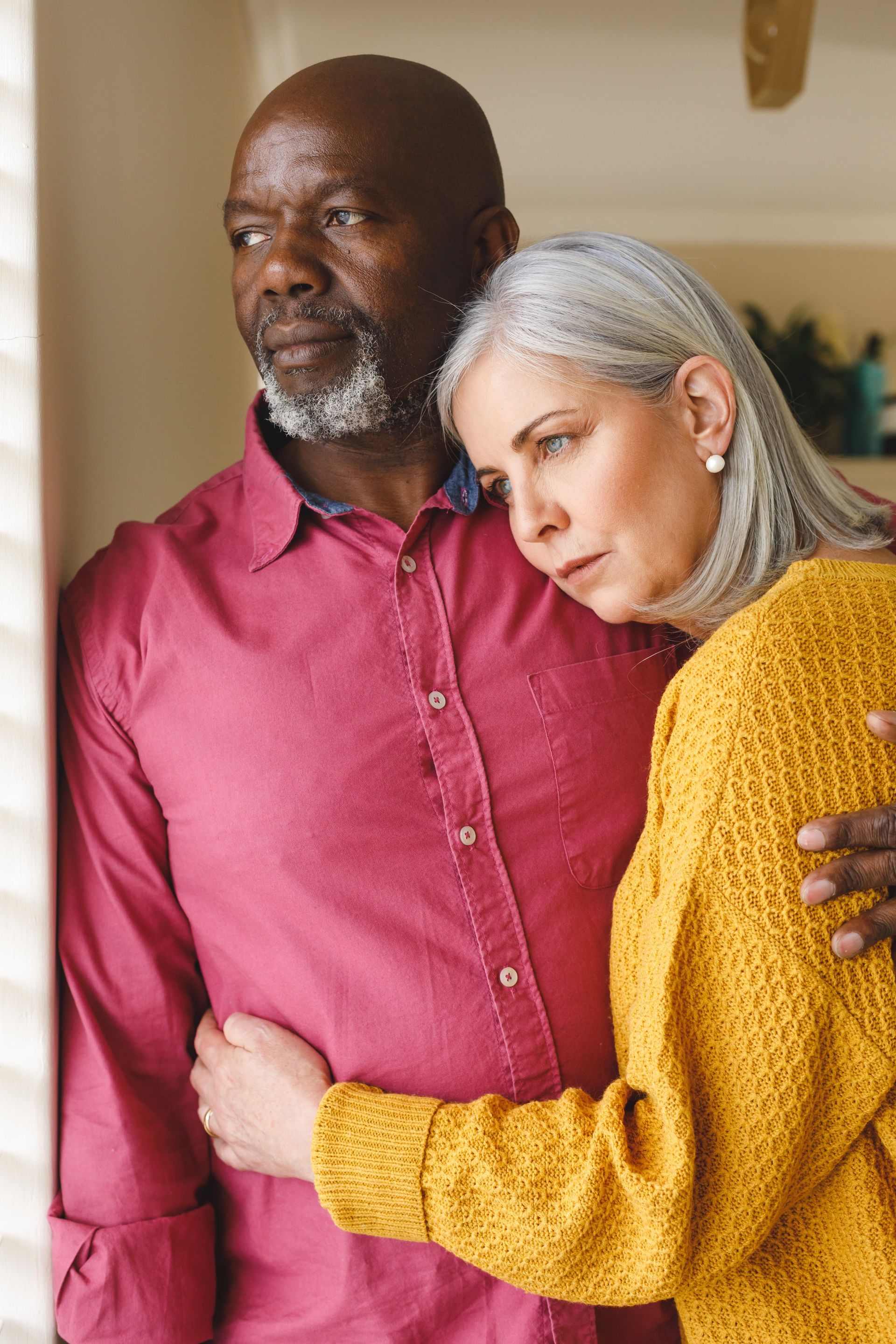 Woman hugs a person with their head on the woman’s shoulder. Both have somber expressions.