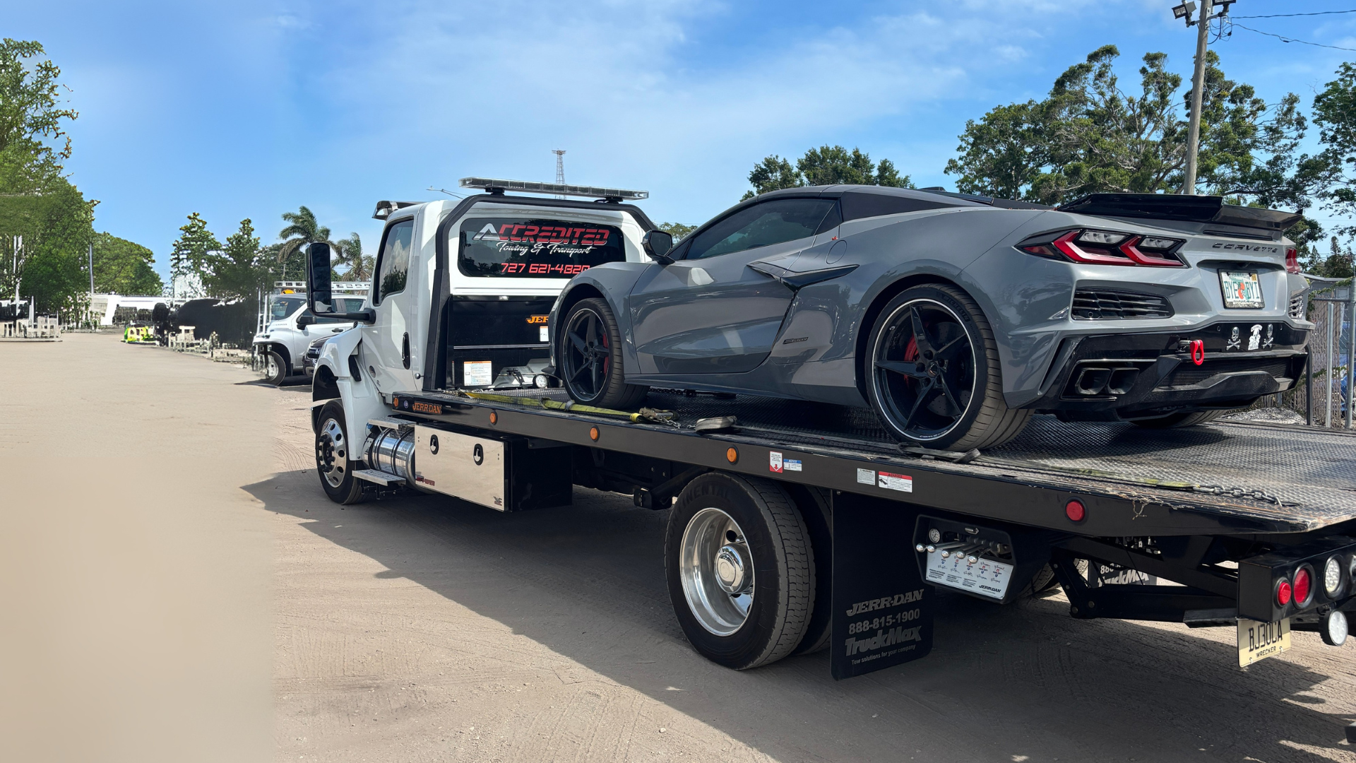Gray sports car on a tow truck, parked on a gravel road under a blue sky.