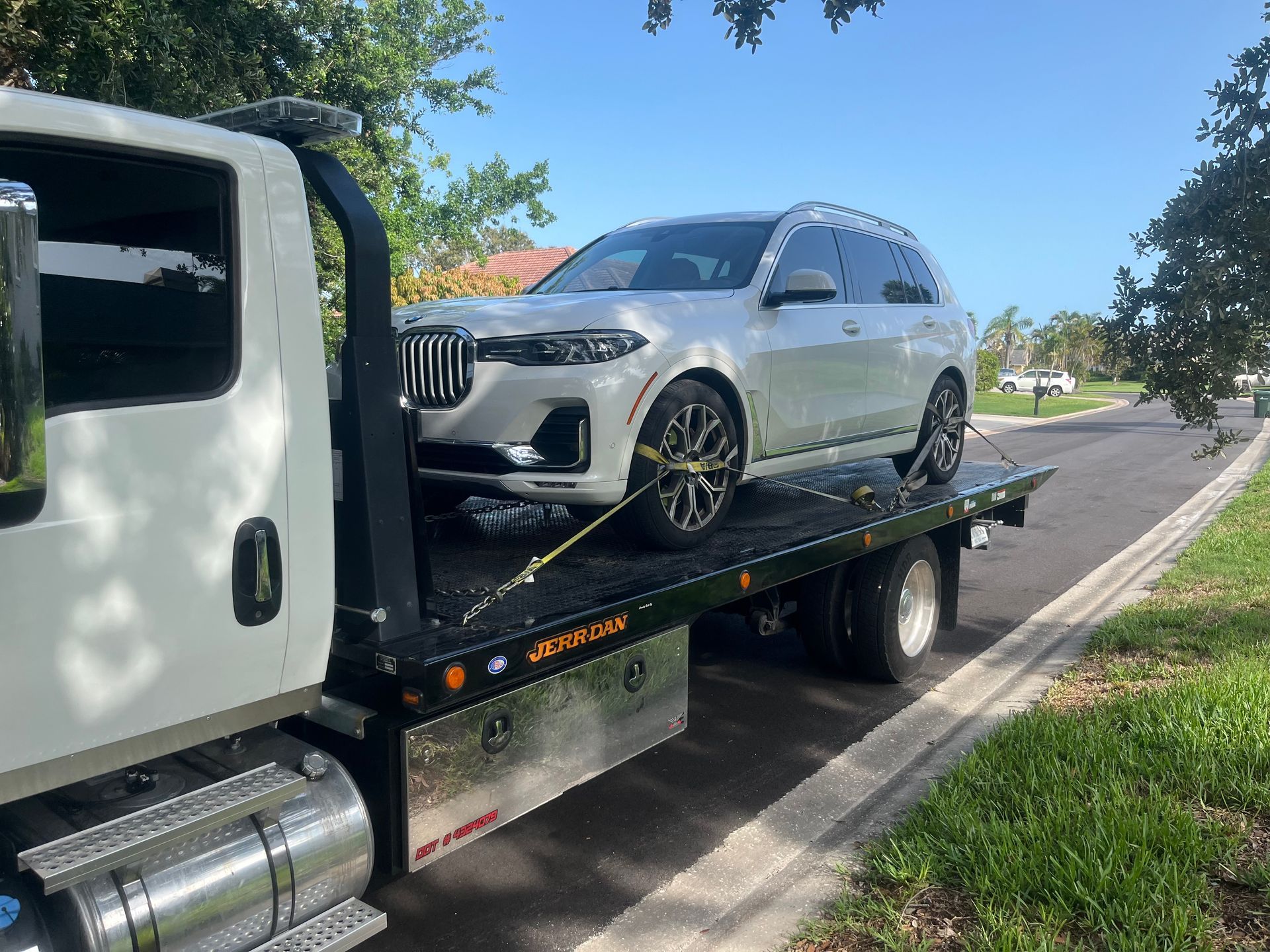 White BMW SUV loaded on a flatbed tow truck on a sunny road.