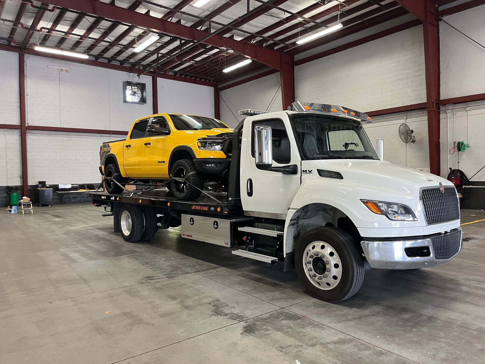 Yellow pickup truck being towed by a white tow truck inside a large building.
