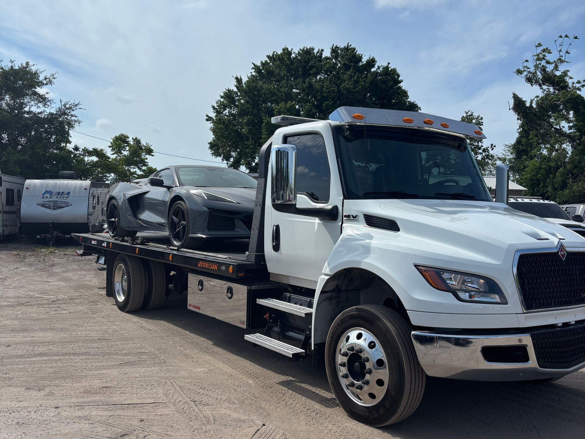 White tow truck hauling a gray sports car outdoors on a sunny day.