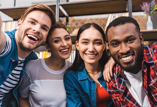 Four smiling people take a selfie; two have arms around others.