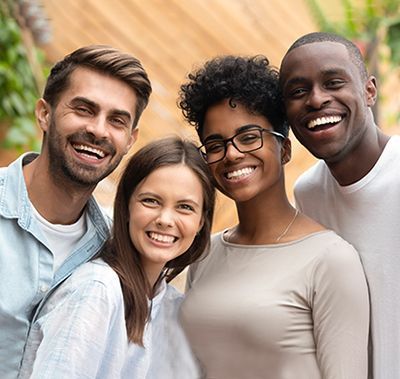 Four diverse people smiling at the camera, posing outdoors.