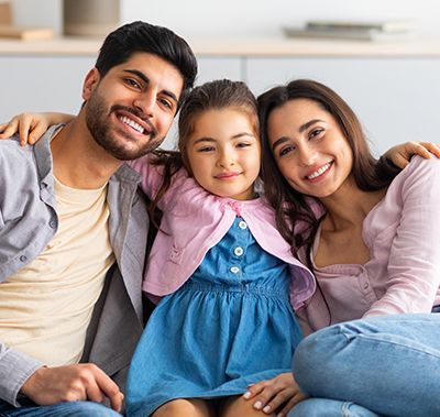 Family smiling, seated indoors. Man and woman have arms around a young child.