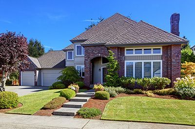 Two-story house with red brick facade, gray siding, and a landscaped front yard with green lawn.