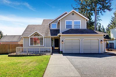 Two-story house with a light gray exterior, two-car garage, and a green lawn under a bright blue sky.