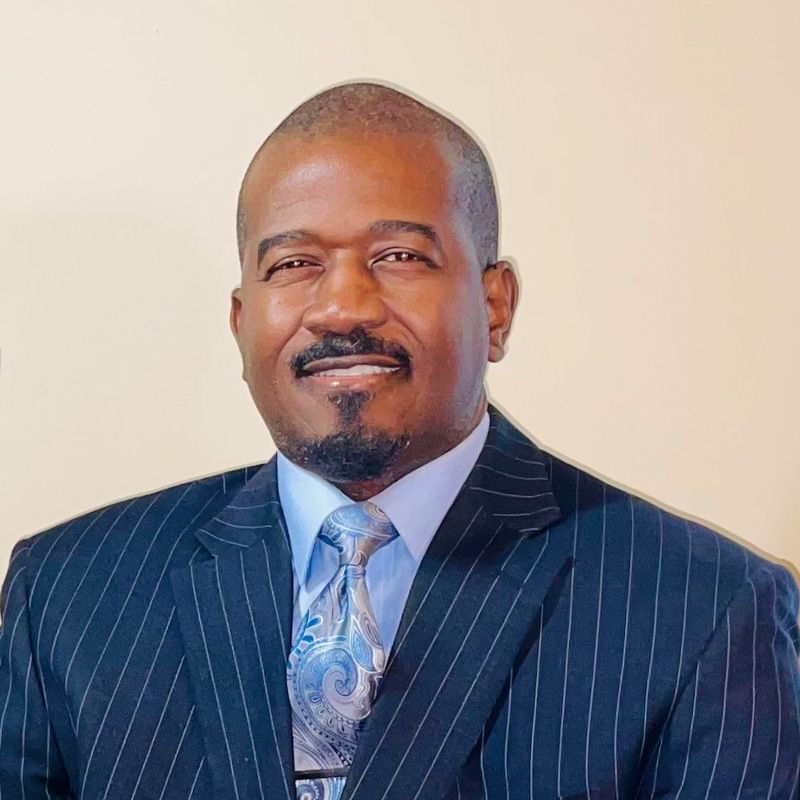 Man in a pinstripe suit and tie smiles, chest up portrait, beige background.
