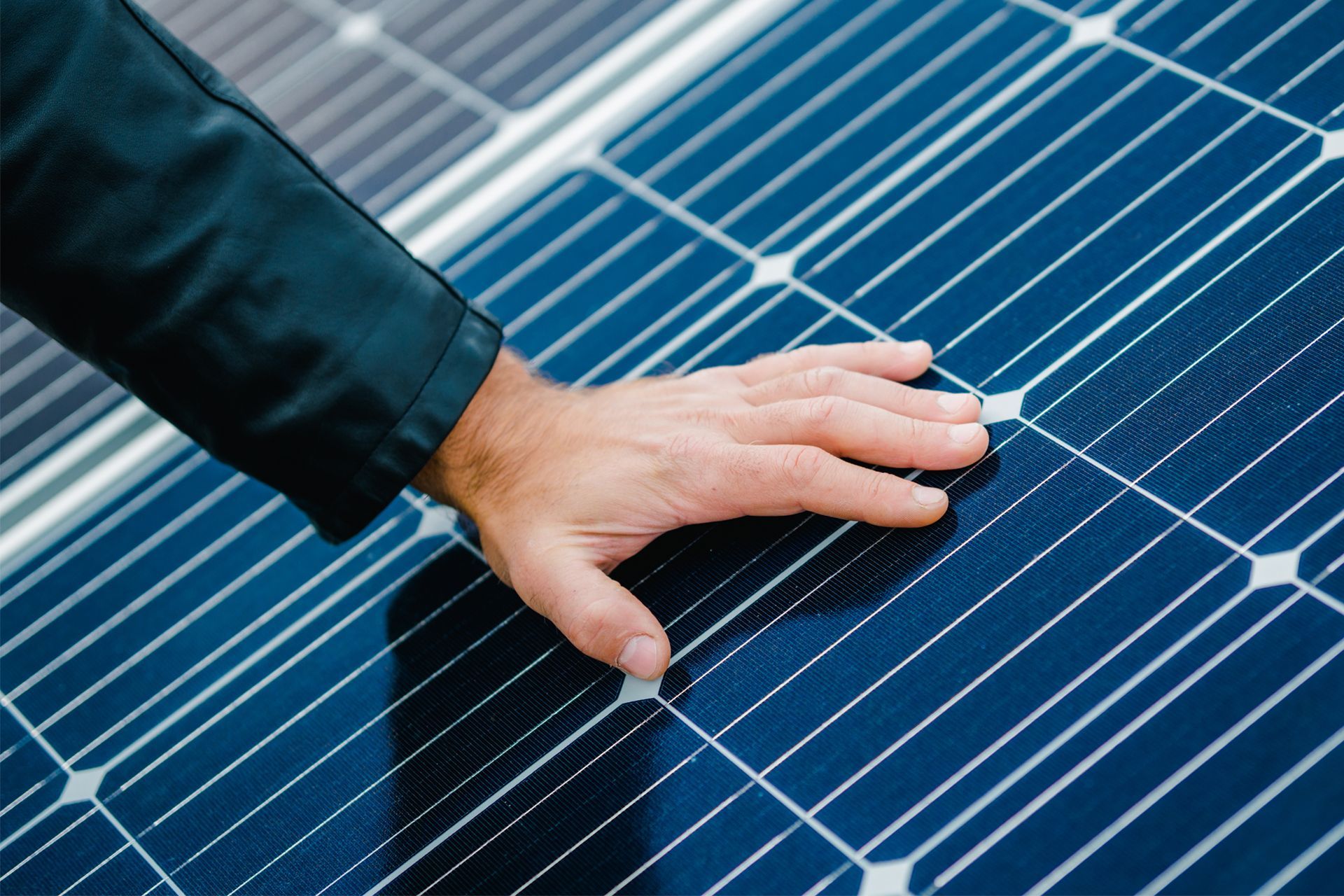 A hand touching a blue solar panel, inspecting its surface.