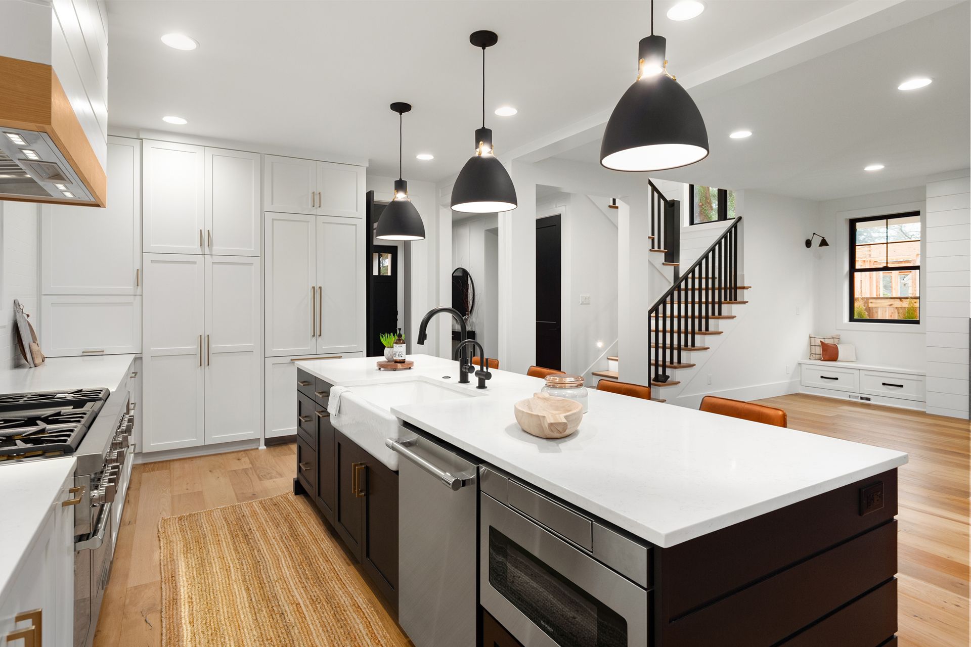 Modern kitchen with white cabinets, dark island, pendant lights, and a staircase.