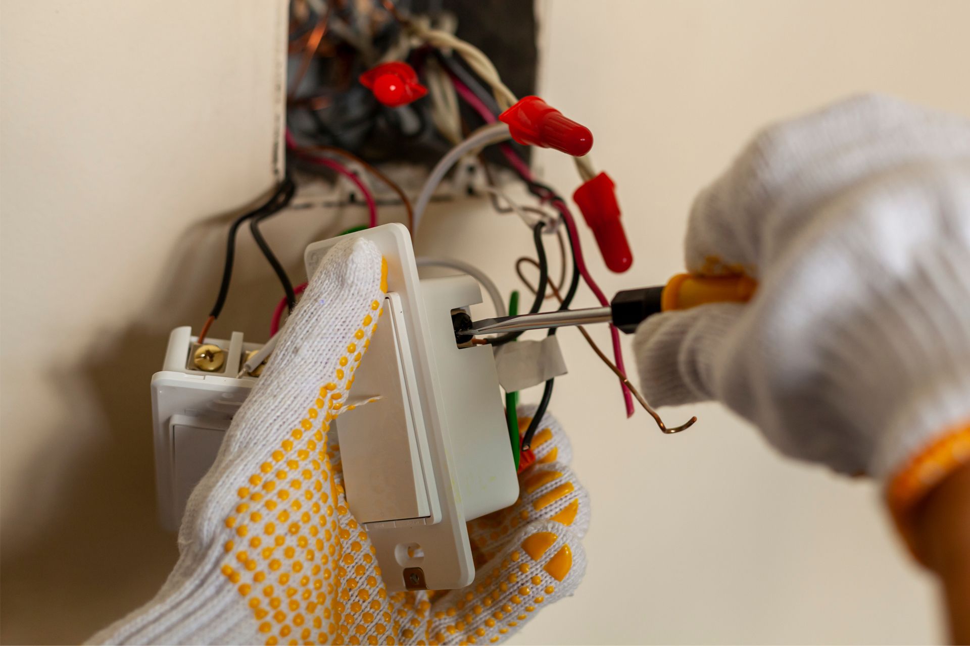 Electrician installing a light switch, hands in gloves with a screwdriver, close-up.