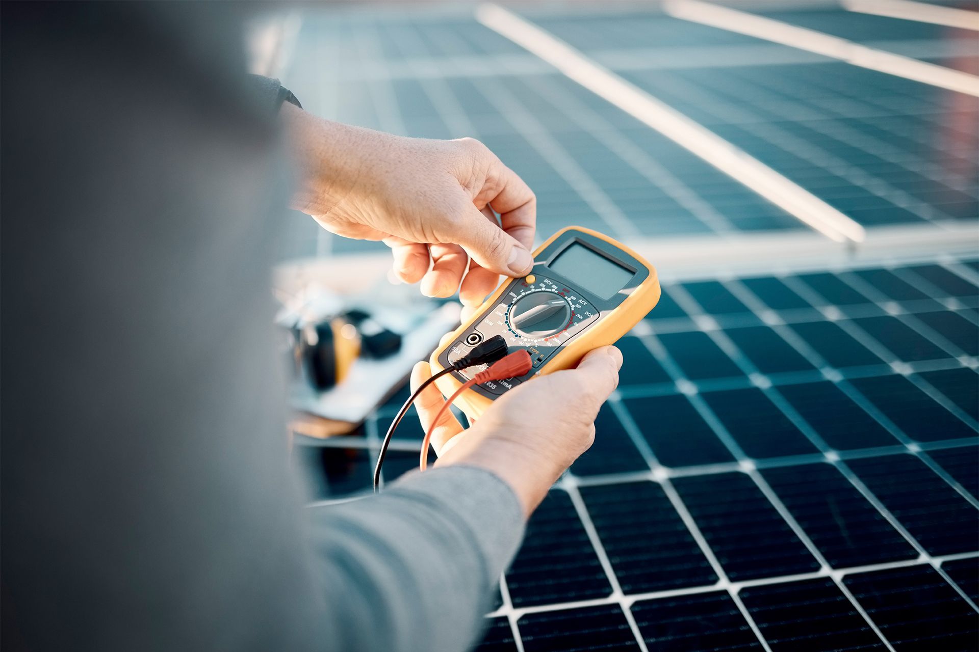 Person using a multimeter to test solar panels on a rooftop.