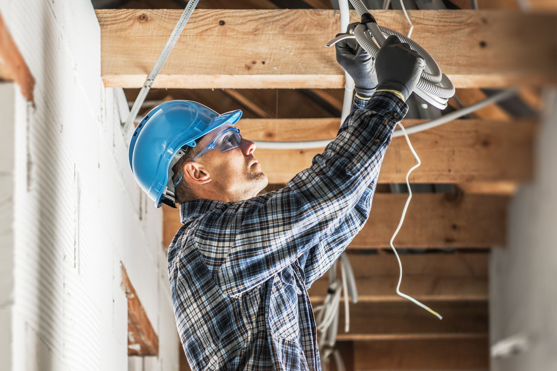 Construction worker in blue hard hat and goggles, installing electrical wiring in a building.