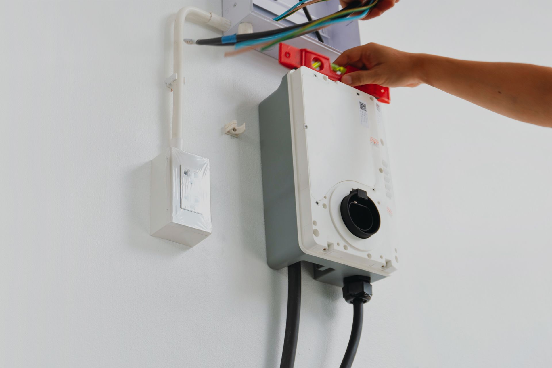 Electrician installing a charging station on a white wall, with exposed wires and tools.