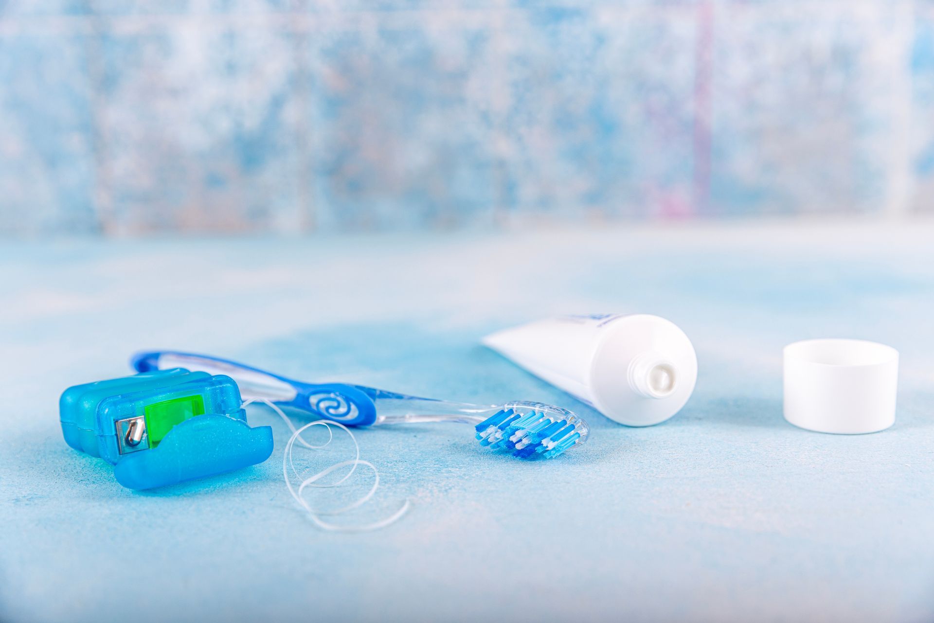 Une brosse à dents, du fil dentaire, du dentifrice et un tube de dentifrice sur une table bleue.