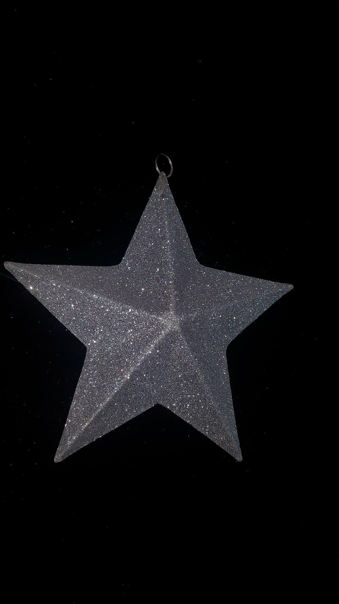 Adorno de estrella gris brillante de cinco puntas colgando sobre un fondo negro.