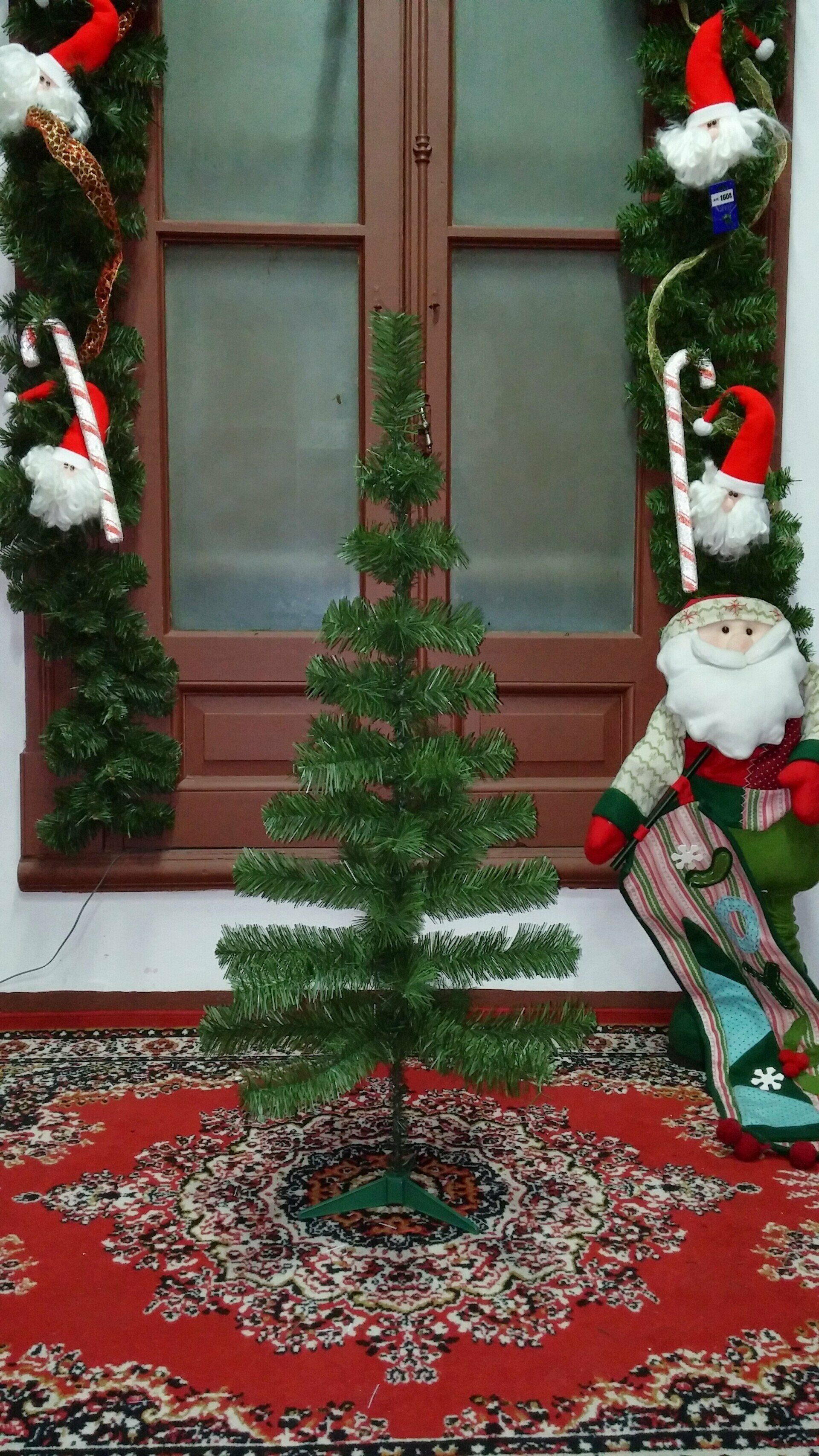 Un pequeño árbol de Navidad sobre una alfombra roja estampada, junto a una ventana decorada y ositos de peluche navideños.