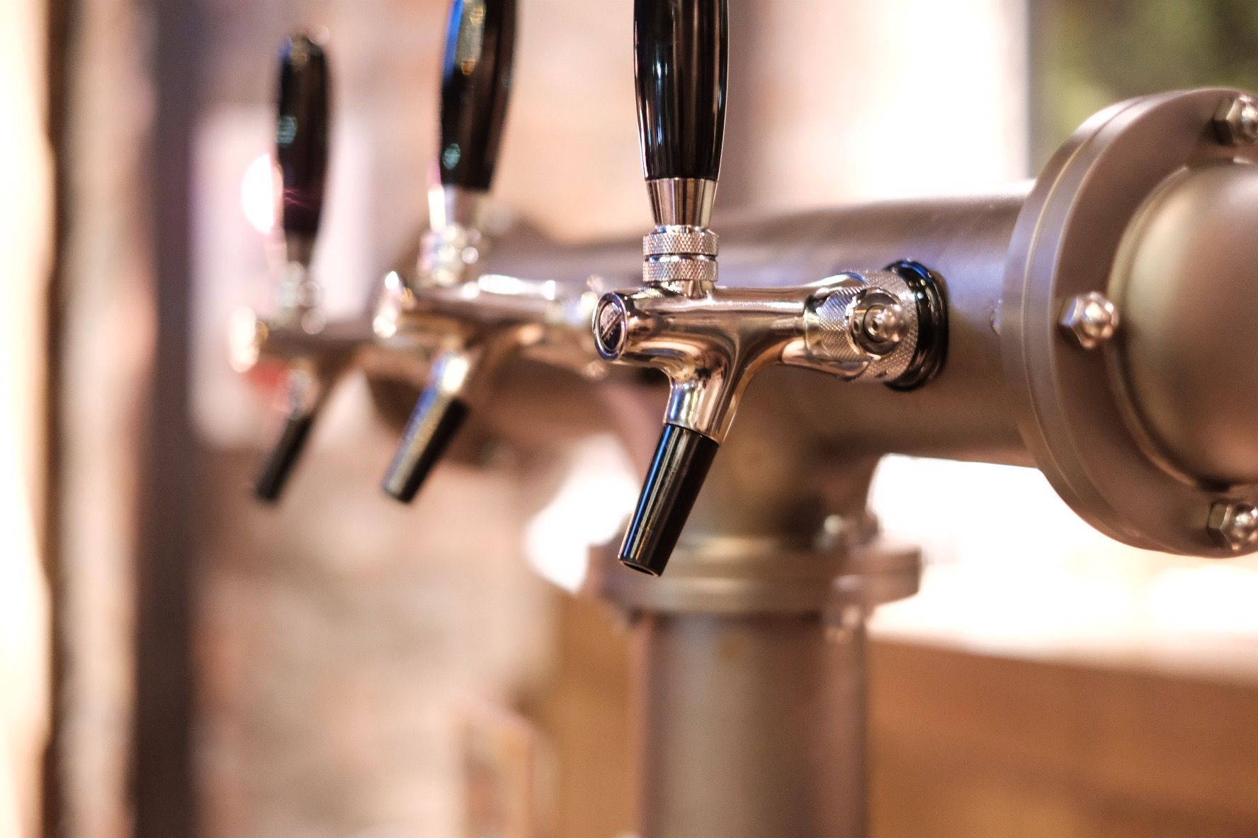Close-up of three beer taps on a stainless steel fixture.