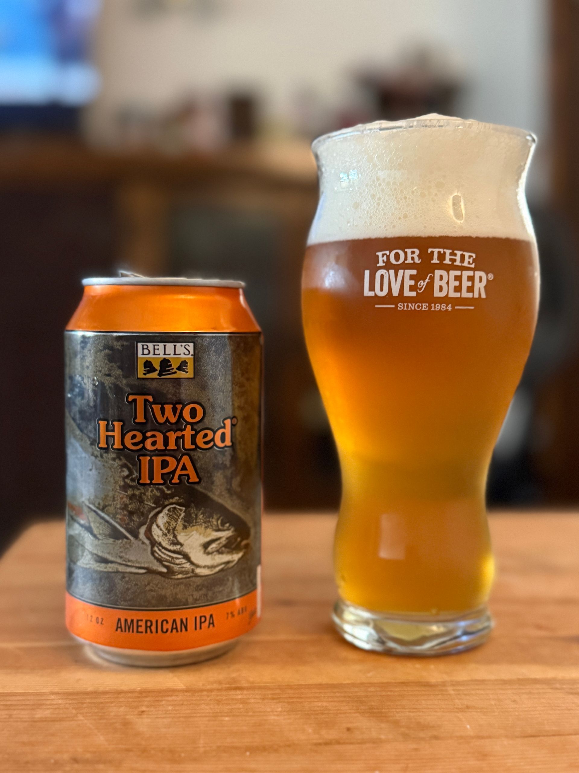 A can and a glass of Two Hearted IPA beer on a wooden surface.