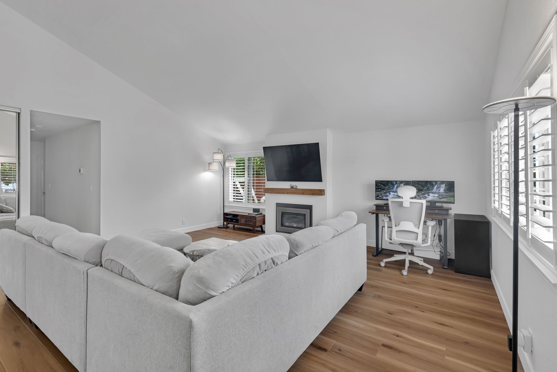 Bright, modern living room with gray sectional, TV, and home office setup.