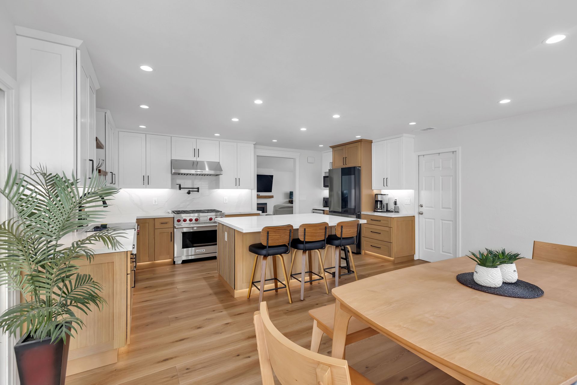 Modern kitchen with wood floors, white cabinets, island with stools, and dining table.