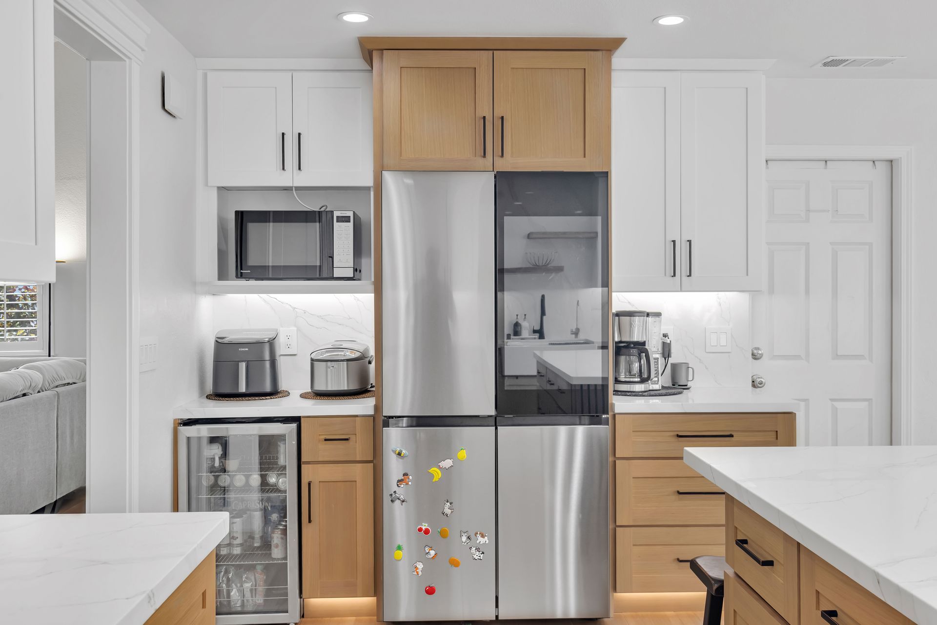 Kitchen with stainless steel refrigerator, light wood cabinets, white countertops, and white and light brown walls.