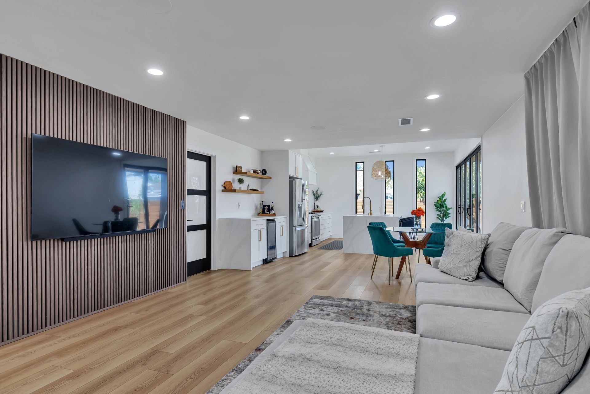 Open-concept living room with TV on a wood-paneled wall, couch, dining area, and sliding glass doors.