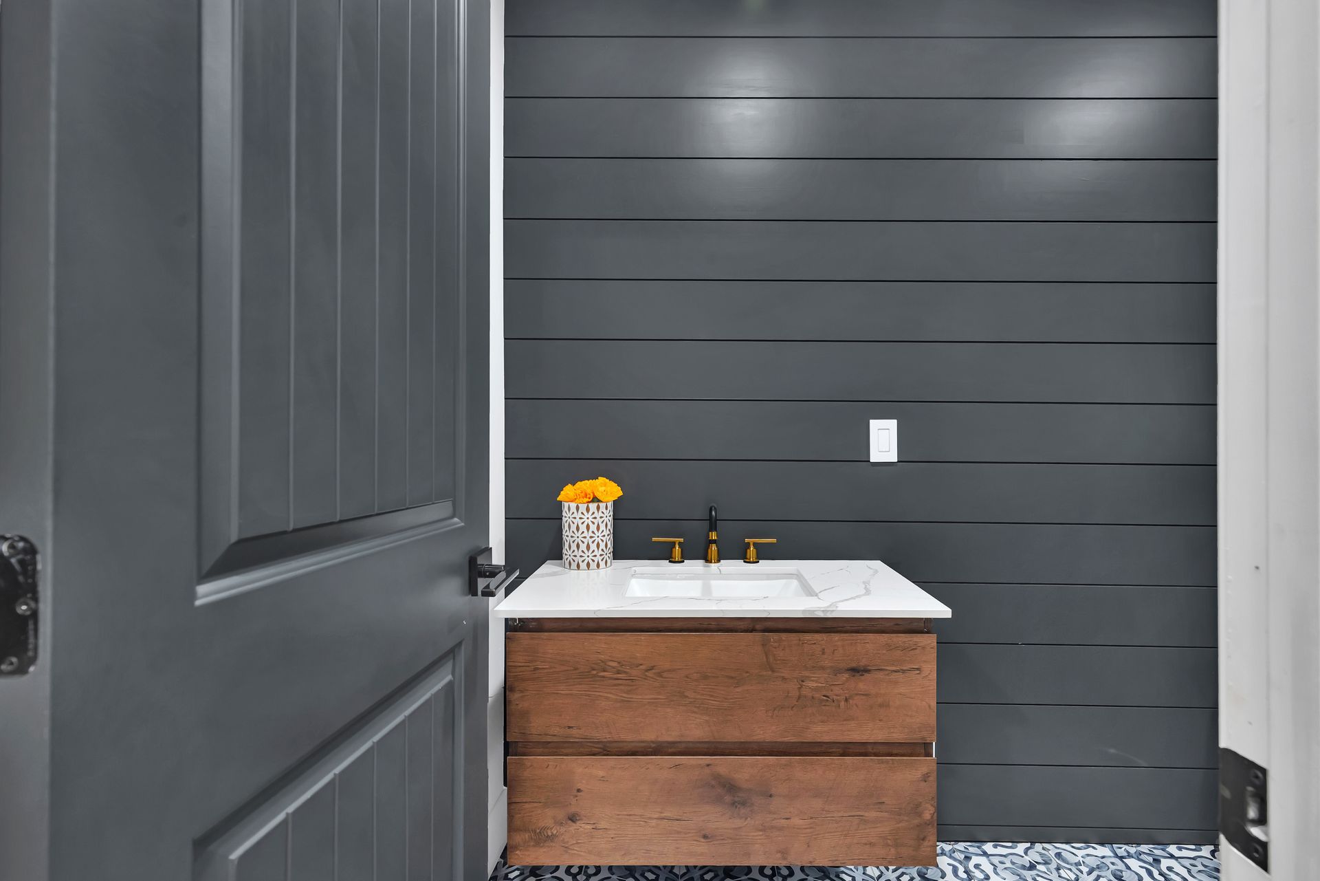 Small bathroom with dark gray shiplap wall, wooden vanity with white countertop, and gray door.