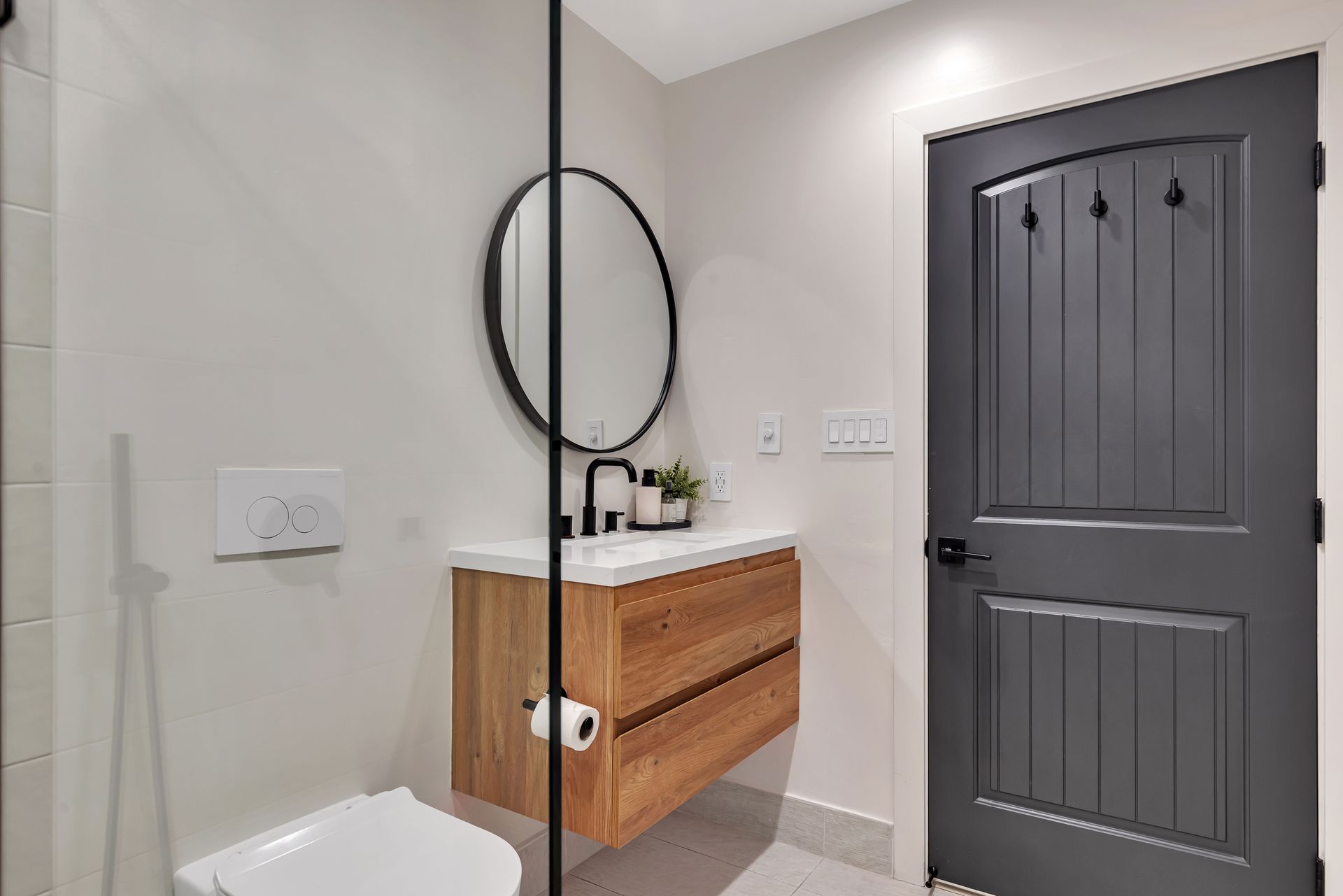 Modern bathroom with wooden vanity, round mirror, and gray door.