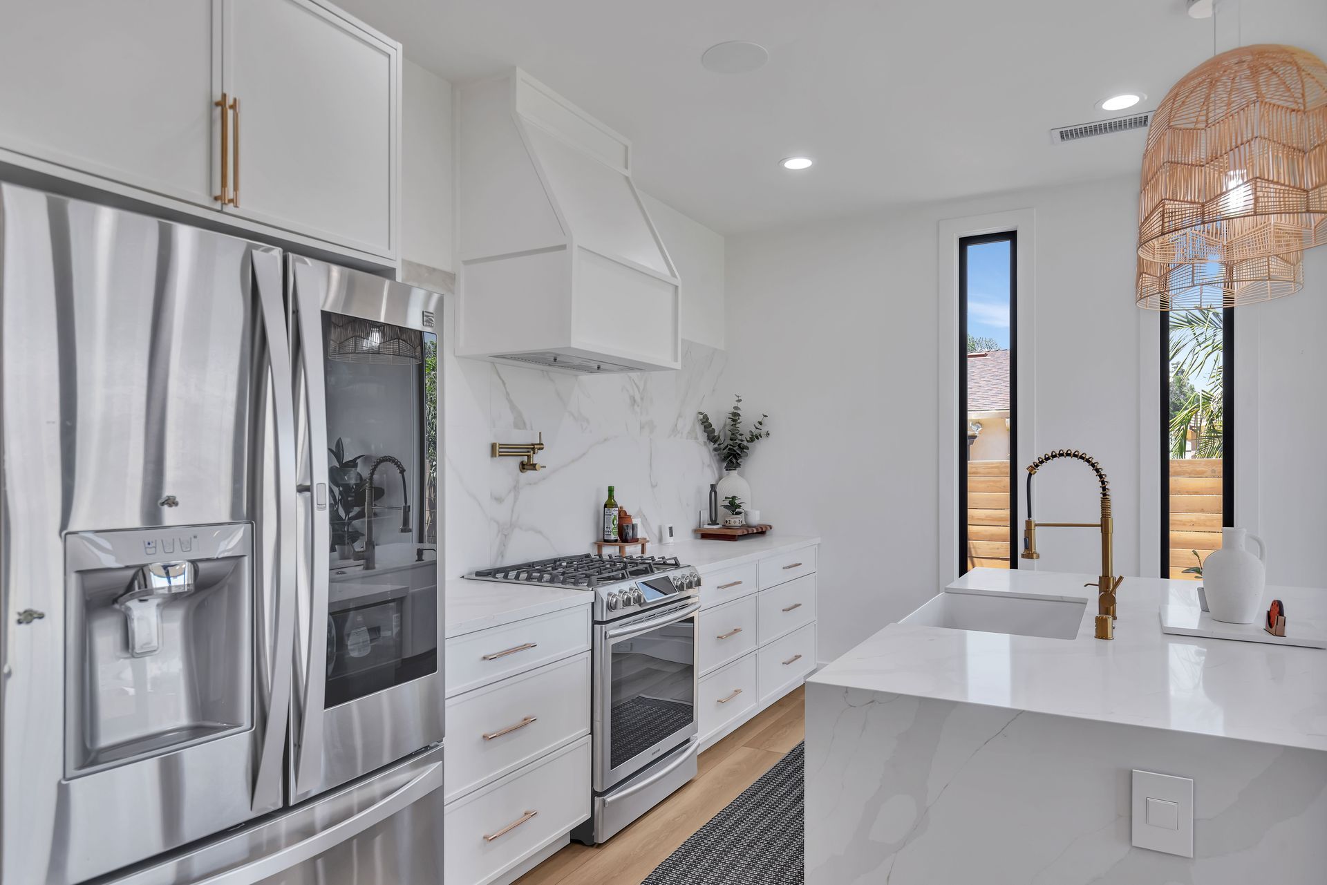 White modern kitchen with stainless steel appliances, marble backsplash, and island with a sink.