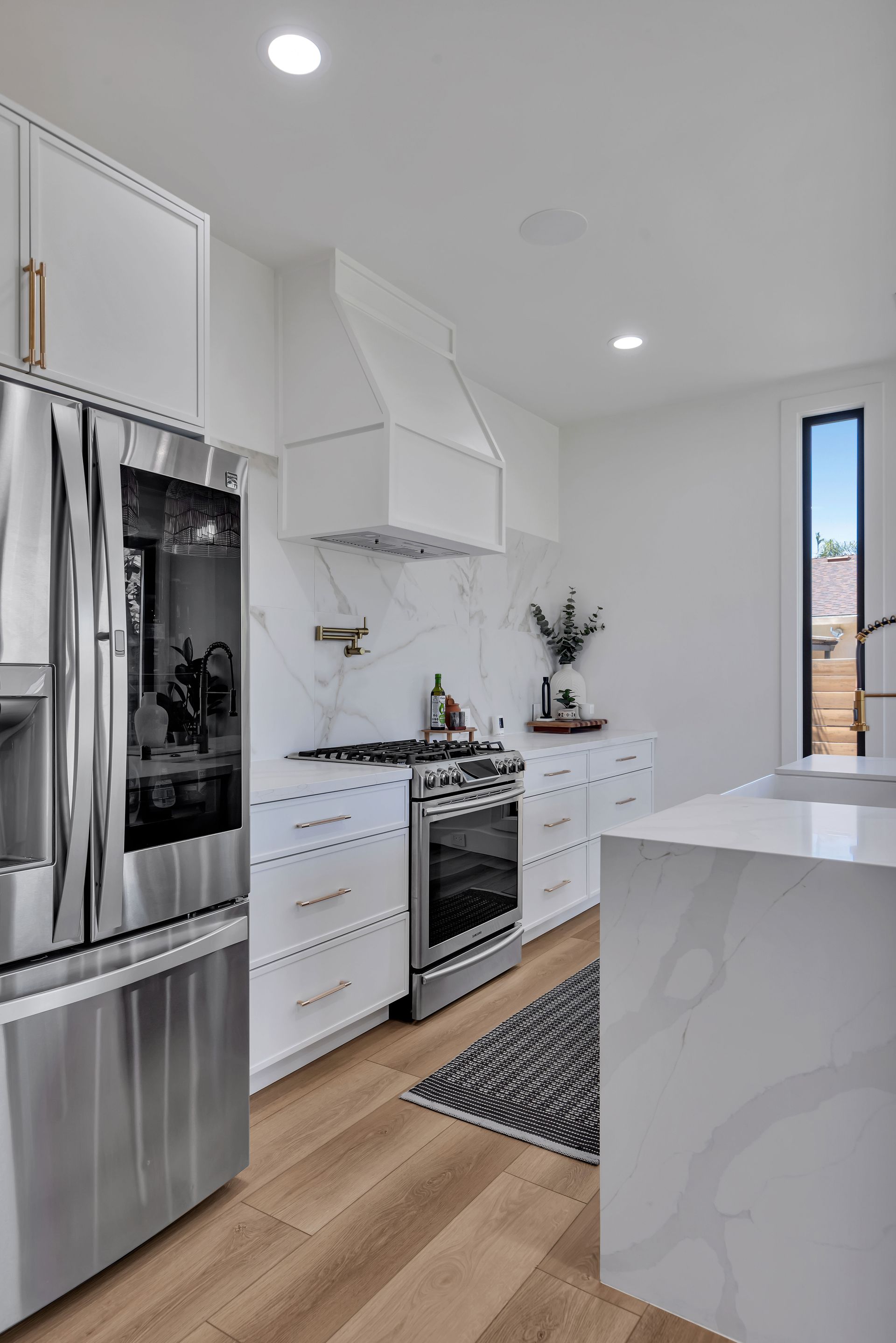 Modern white kitchen with stainless steel appliances, marble backsplash, and a patterned rug.