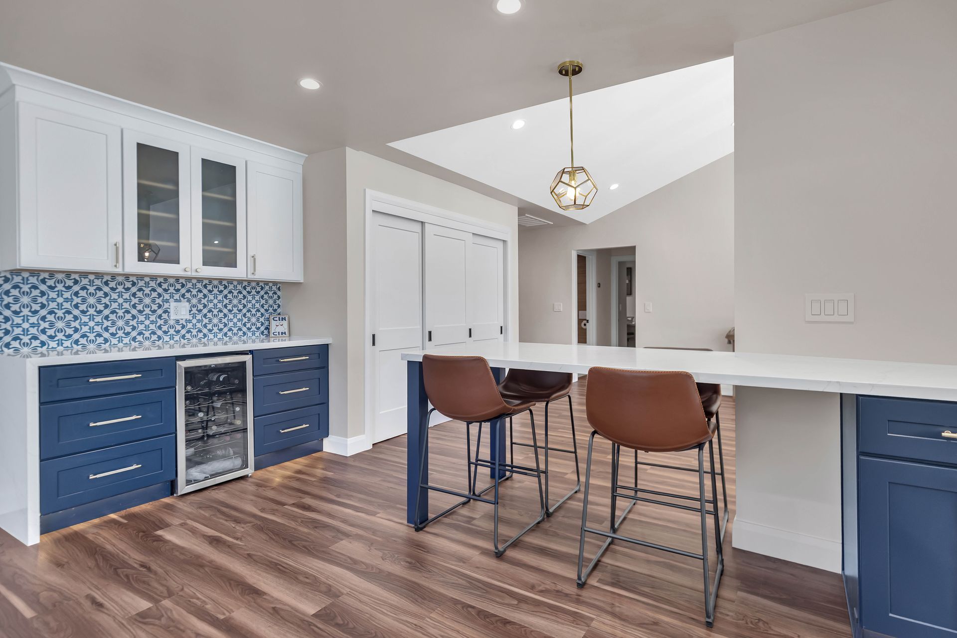 Modern kitchen with blue and white cabinets, breakfast bar with stools, wooden floor, and a hanging light.