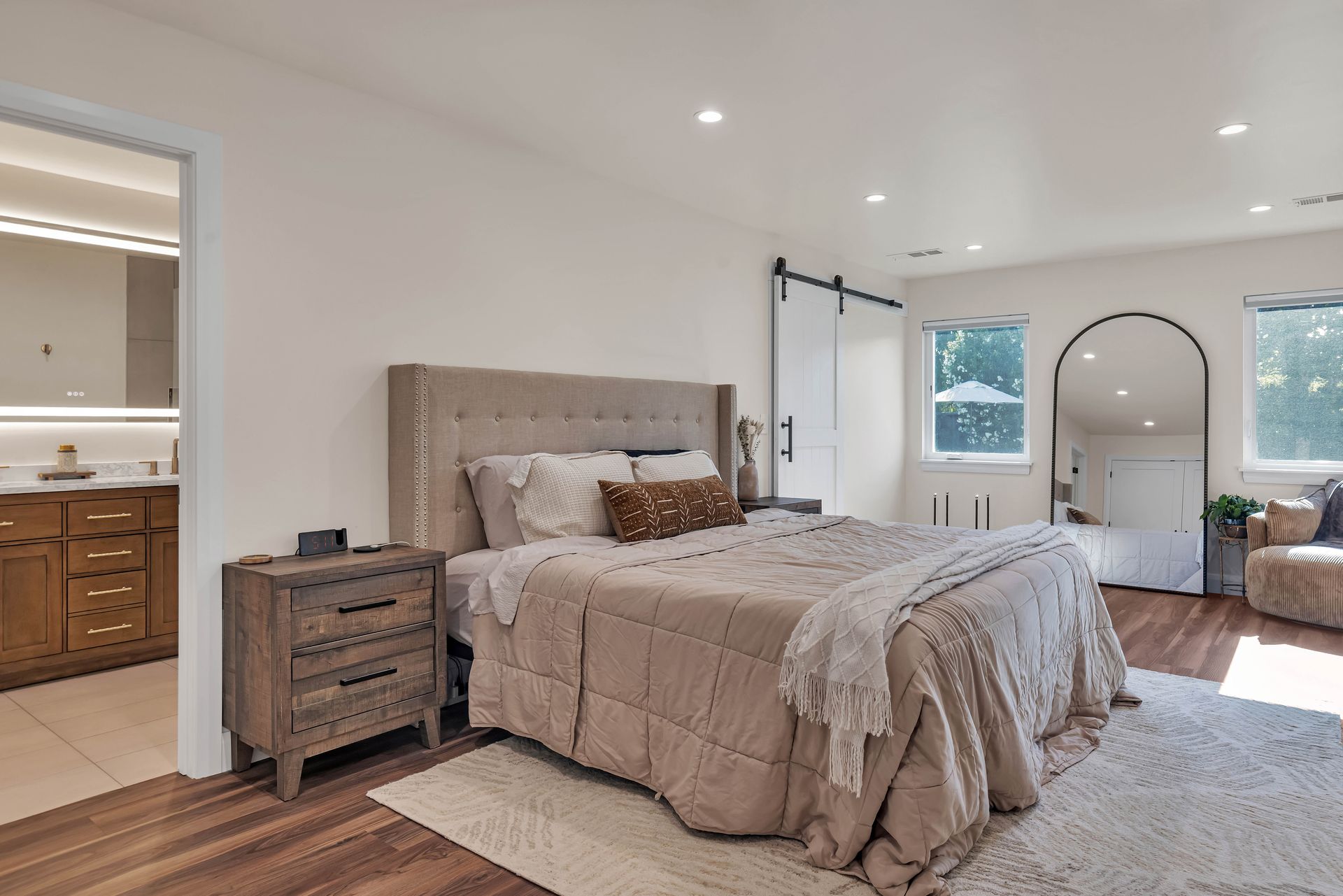 Bedroom with bed, nightstand, sliding door, large mirror, and open doorway to bathroom.