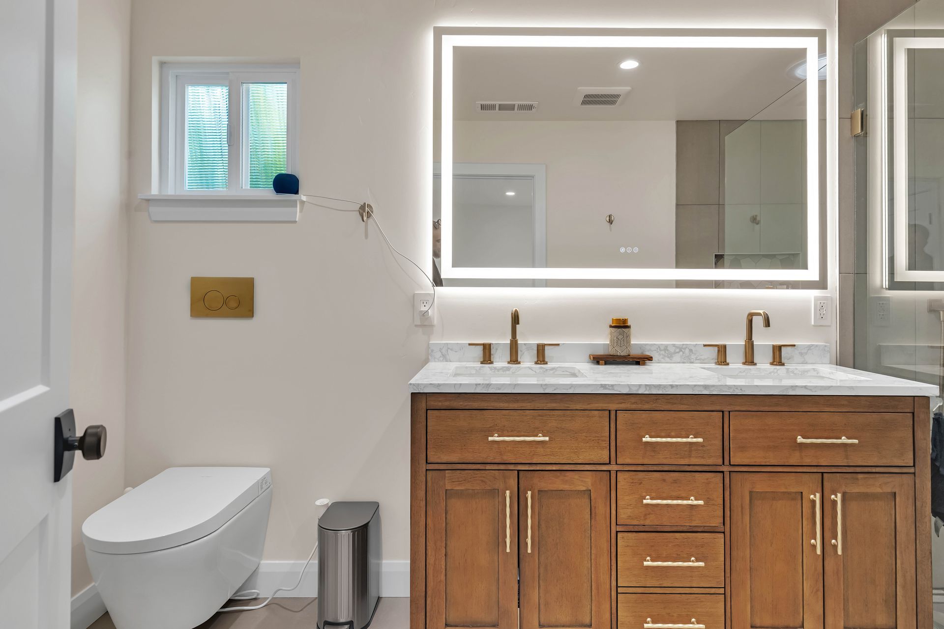 Modern bathroom with a wooden vanity, double sinks, a large mirror with lights, and a white toilet.
