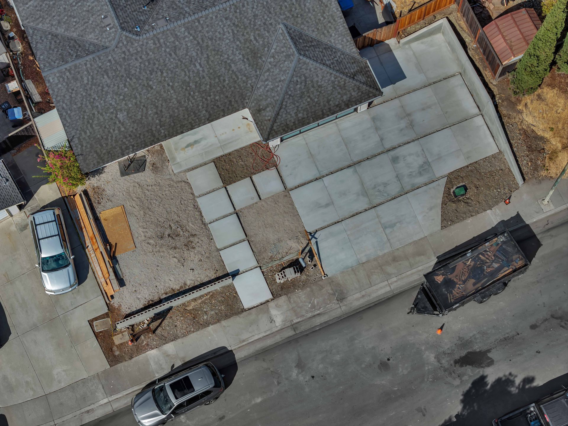Aerial view of a house with gray roof, concrete driveway, and a street with parked cars.