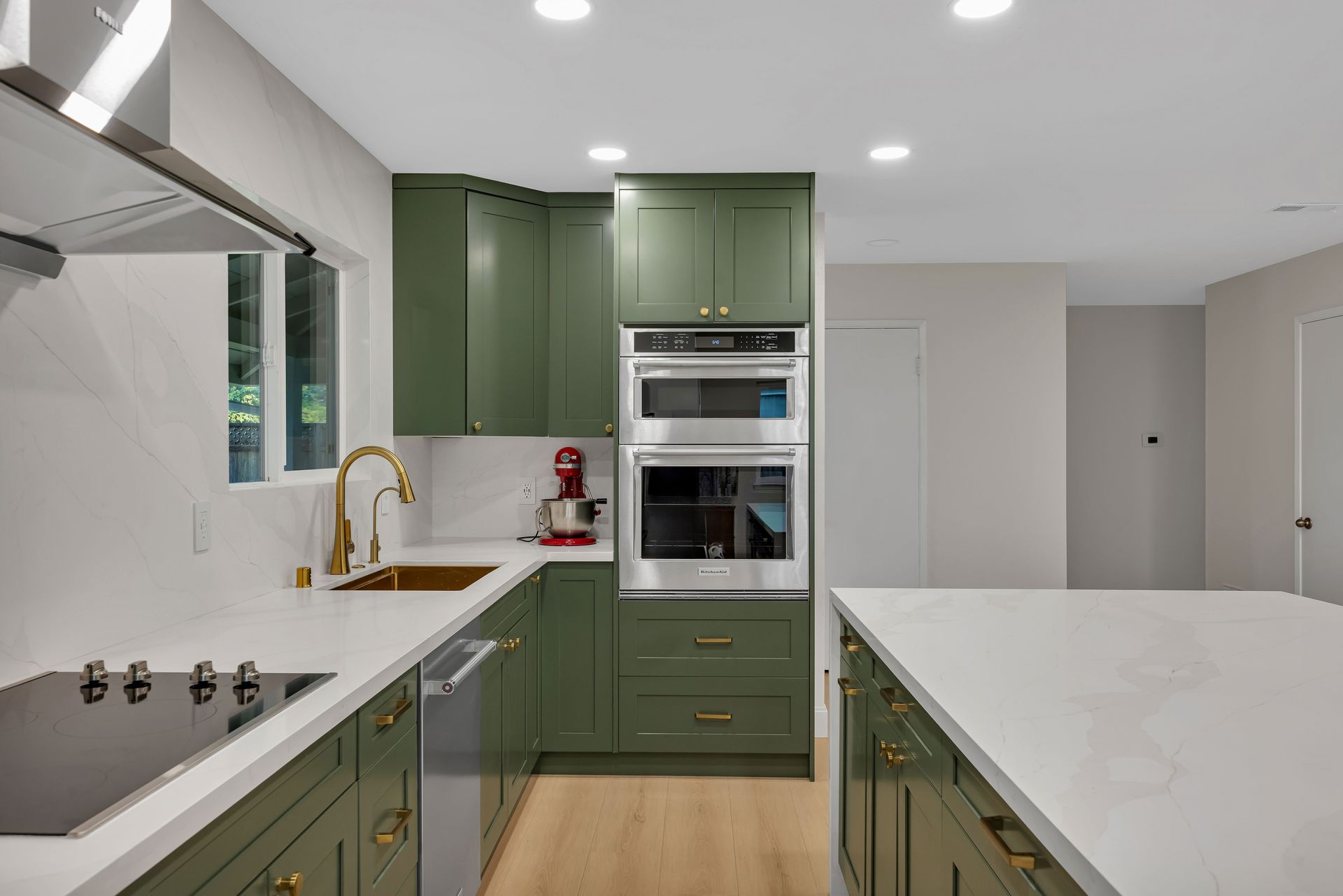 Green kitchen with white countertops, stainless steel appliances, and gold hardware.