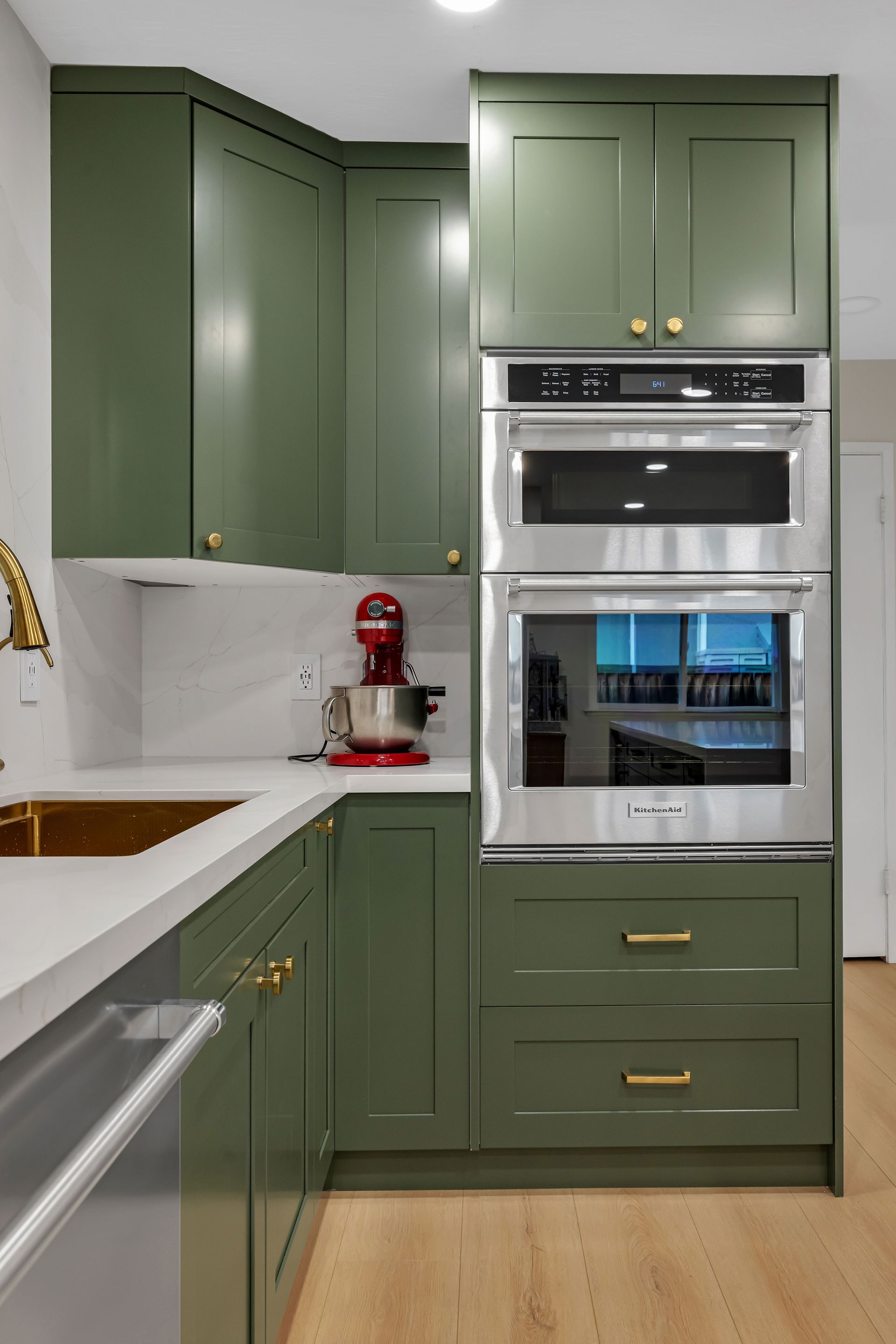 Green kitchen cabinets with built-in stainless steel oven and microwave. Gold hardware.