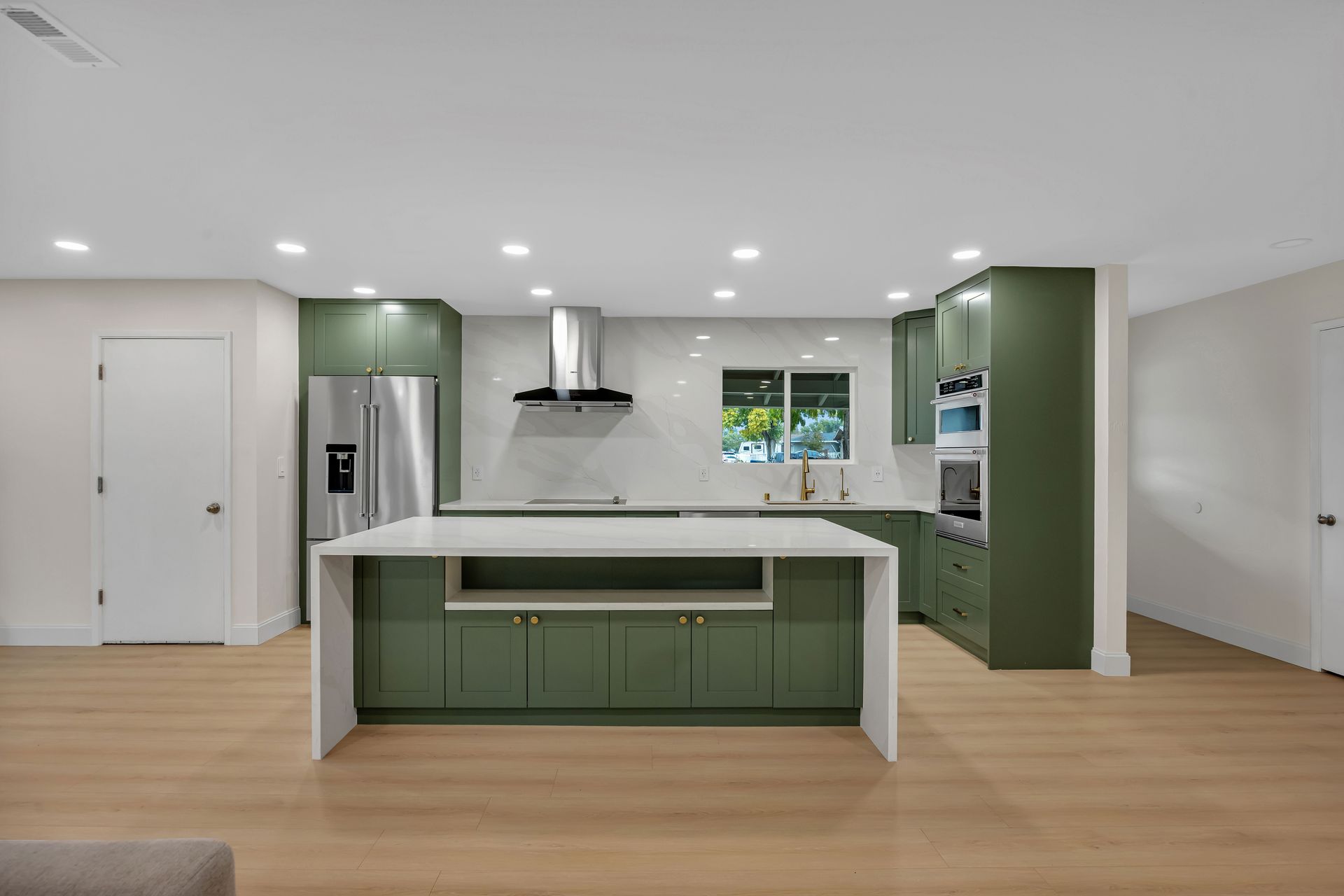 Modern green kitchen with white island, stainless steel appliances, and wood flooring.
