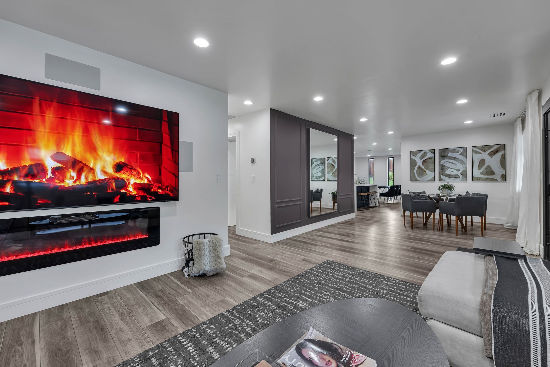 Modern living room with fireplace, TV, and dining area. Gray and white color scheme.