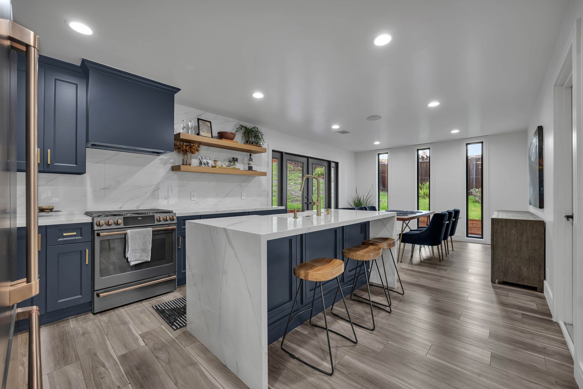 Modern kitchen with navy blue cabinets, marble countertops, and a large island with bar stools.