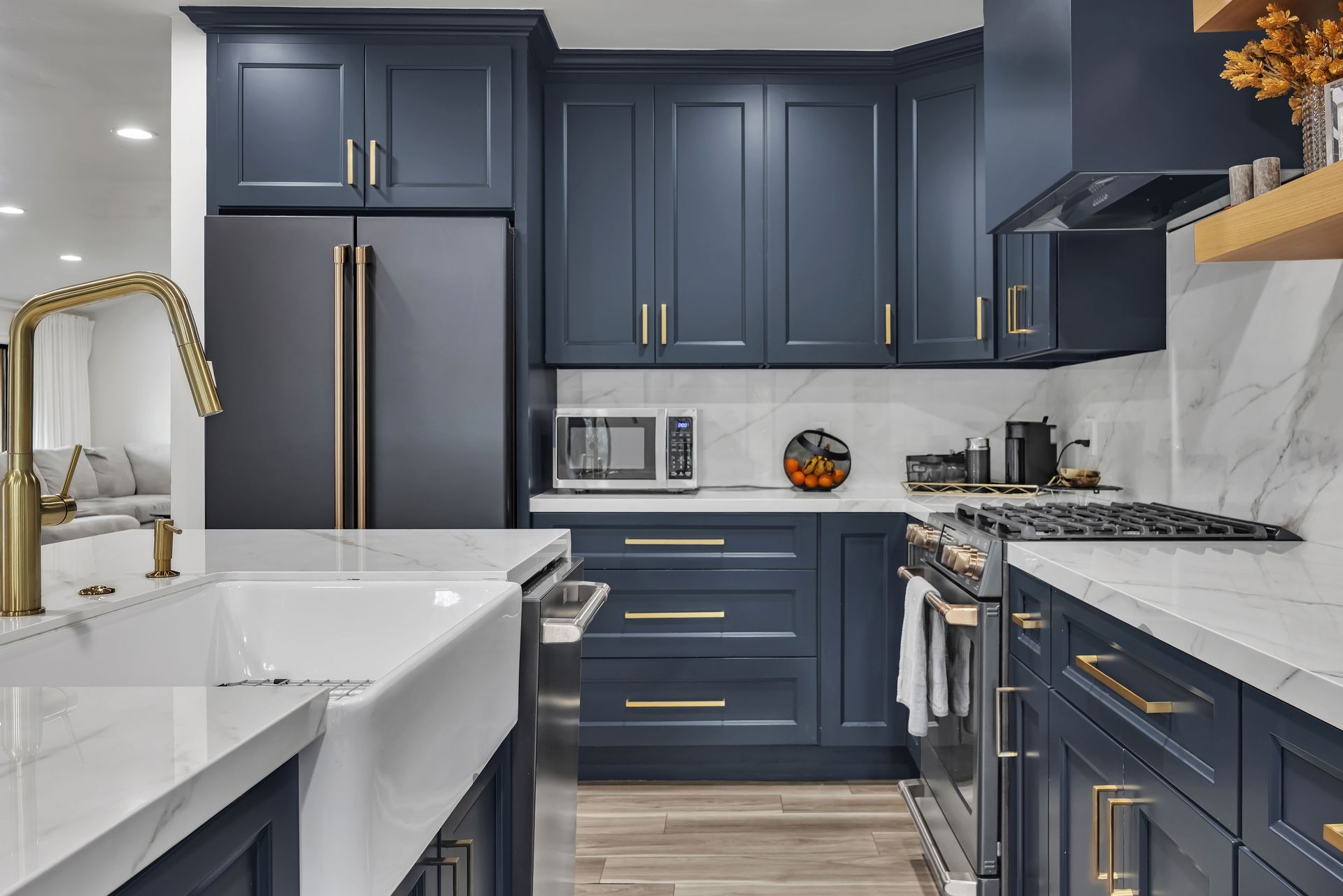 Navy blue kitchen with gold hardware, white countertops, and stainless steel appliances.