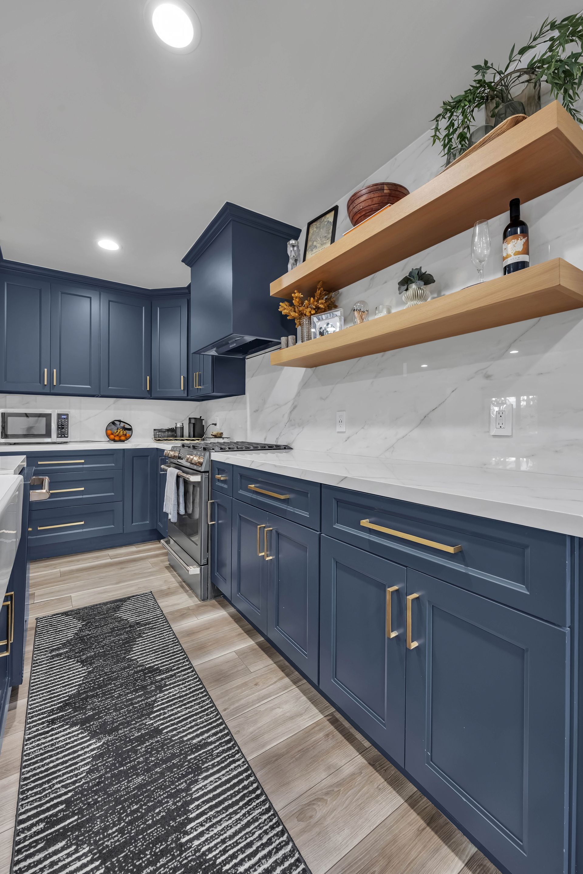 Blue kitchen with white countertops, wooden shelves, and gray and white patterned rug.