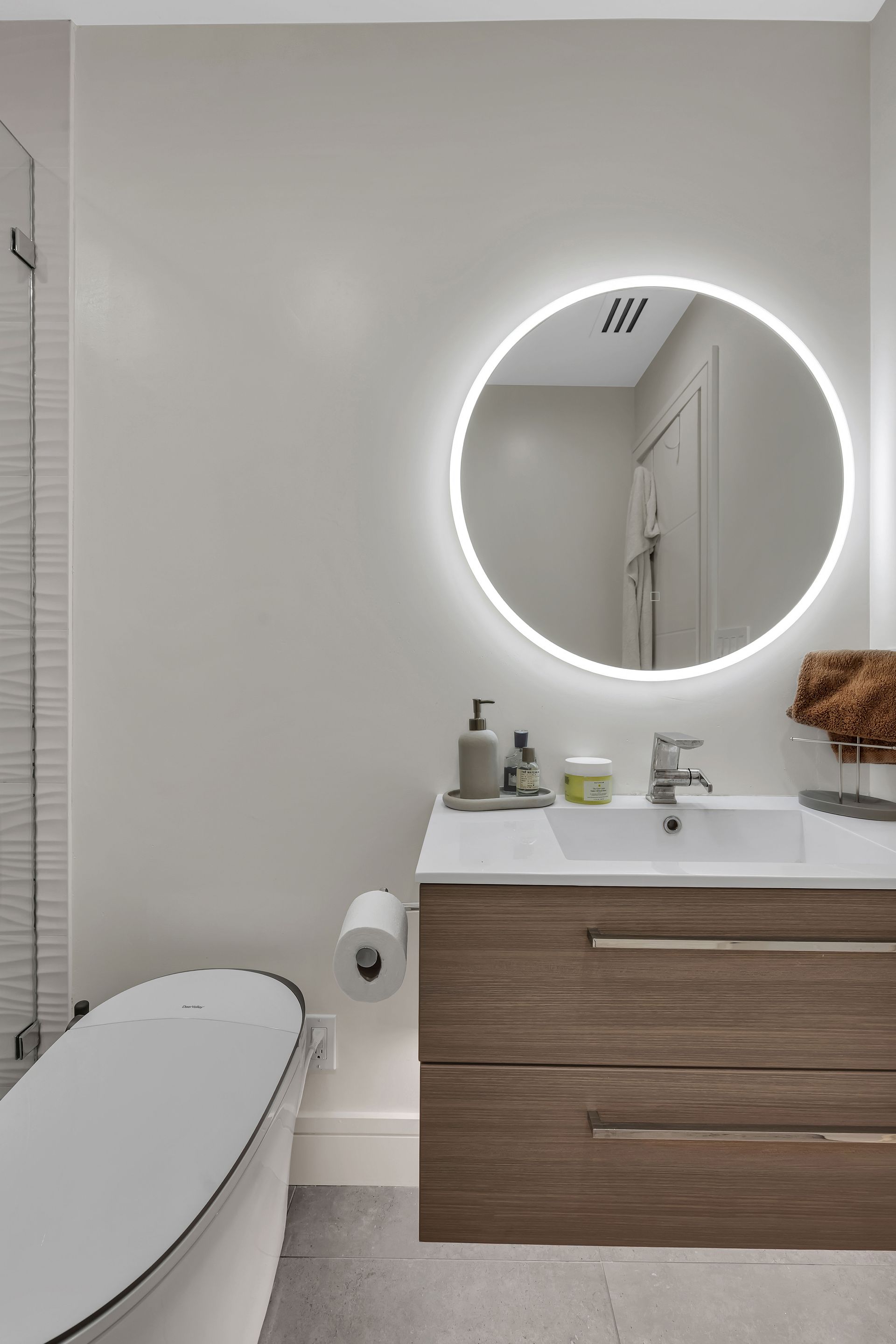 Modern bathroom with a round mirror, wooden vanity, and a toilet.