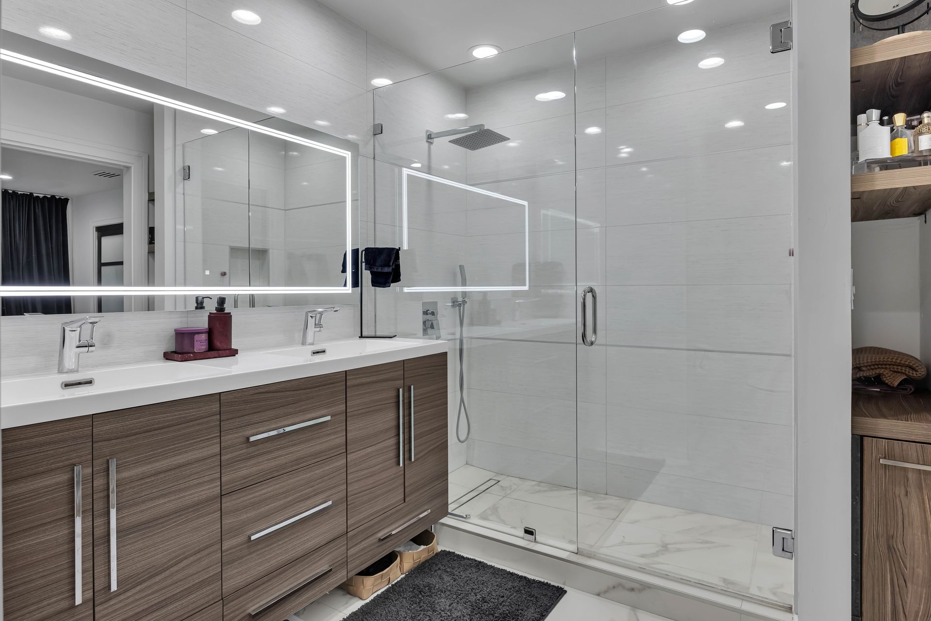 Modern bathroom with glass shower, double vanity, wood cabinets, and white tile.
