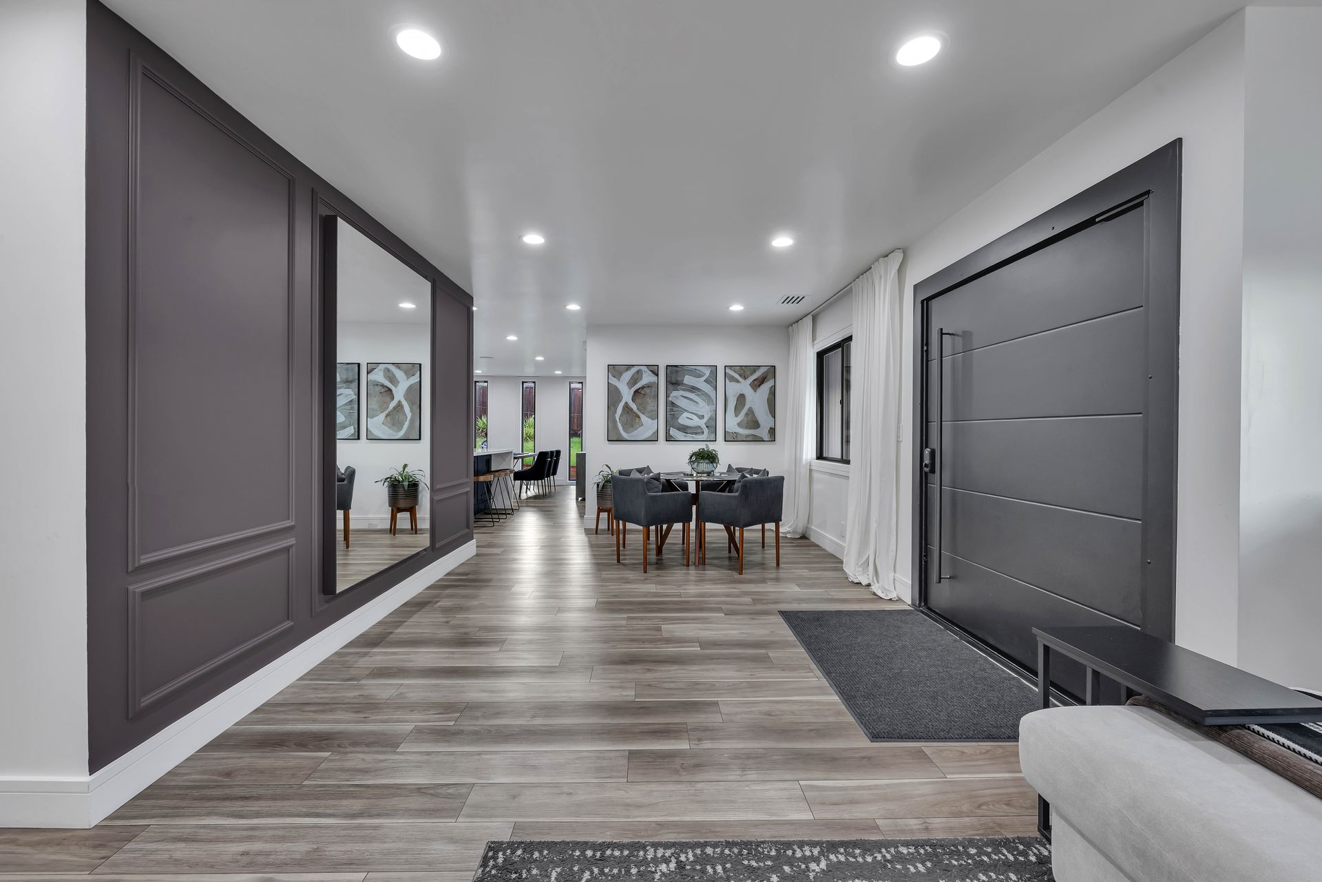 Long hallway with dark gray paneling, large mirror, wooden floors, and dark door.
